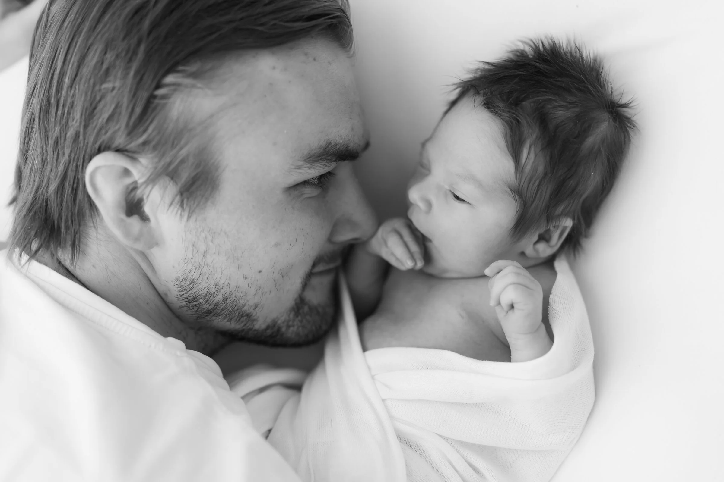 A man gently holding a baby, face to face, looking into each other's eyes in black and white.
