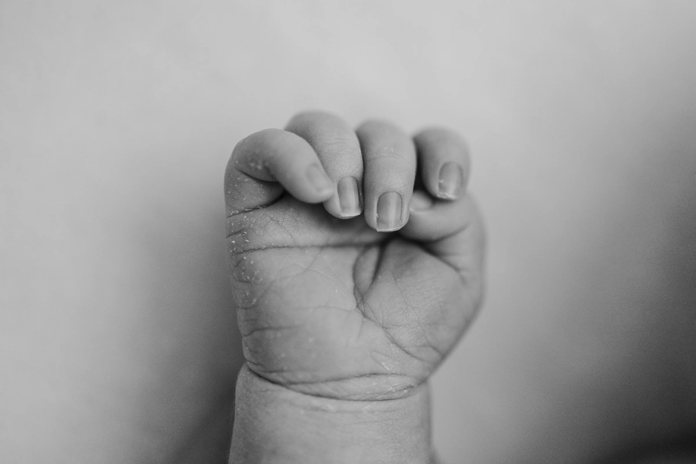 Close-up of a clenched fist of a small child with details of skin and nails visible, captured in black and white.