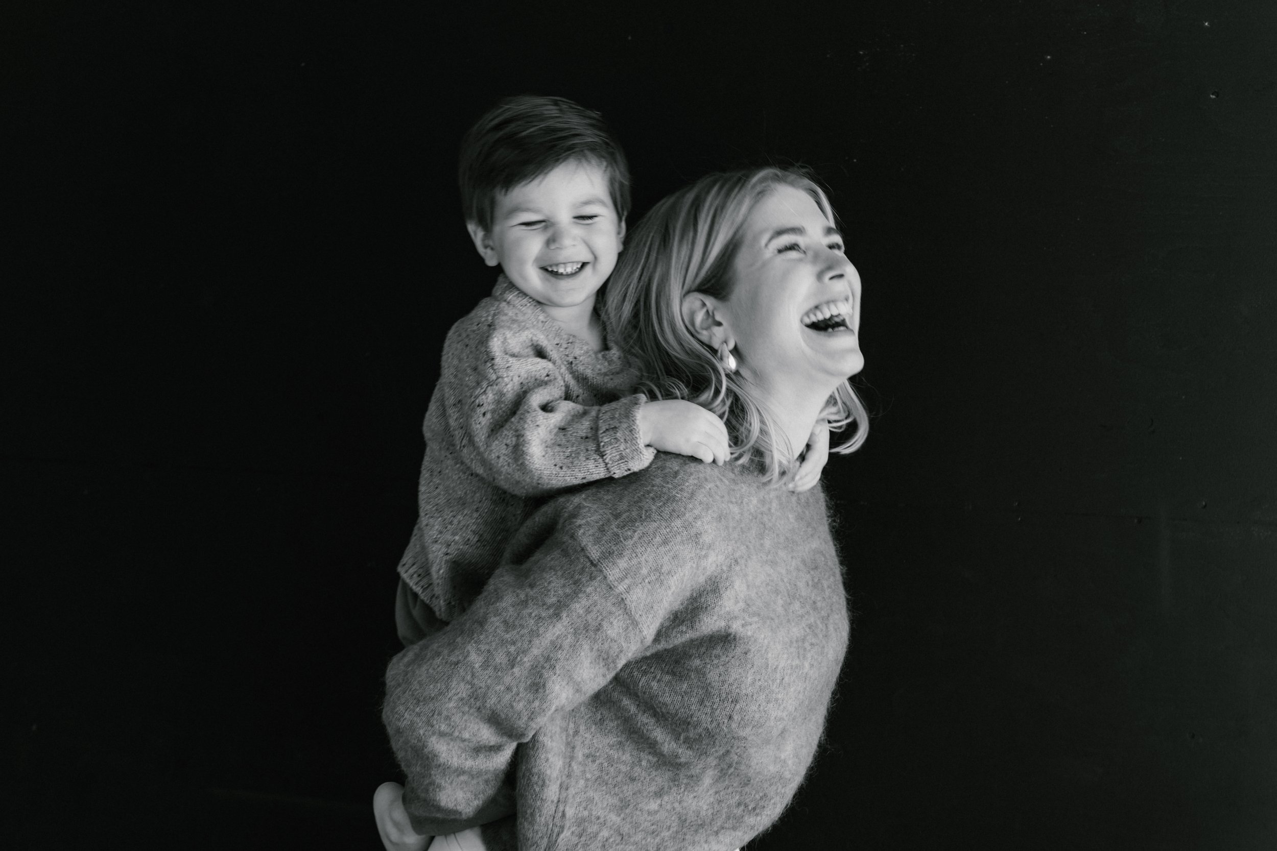 Black and white photo of a woman giving a piggyback ride to a young boy, both laughing and showing joy.