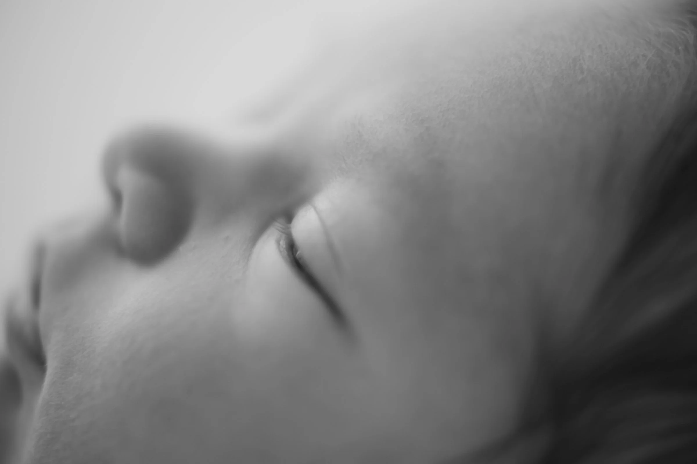 Close-up black and white photo of a sleeping baby's face, focusing on the nose and closed eye.