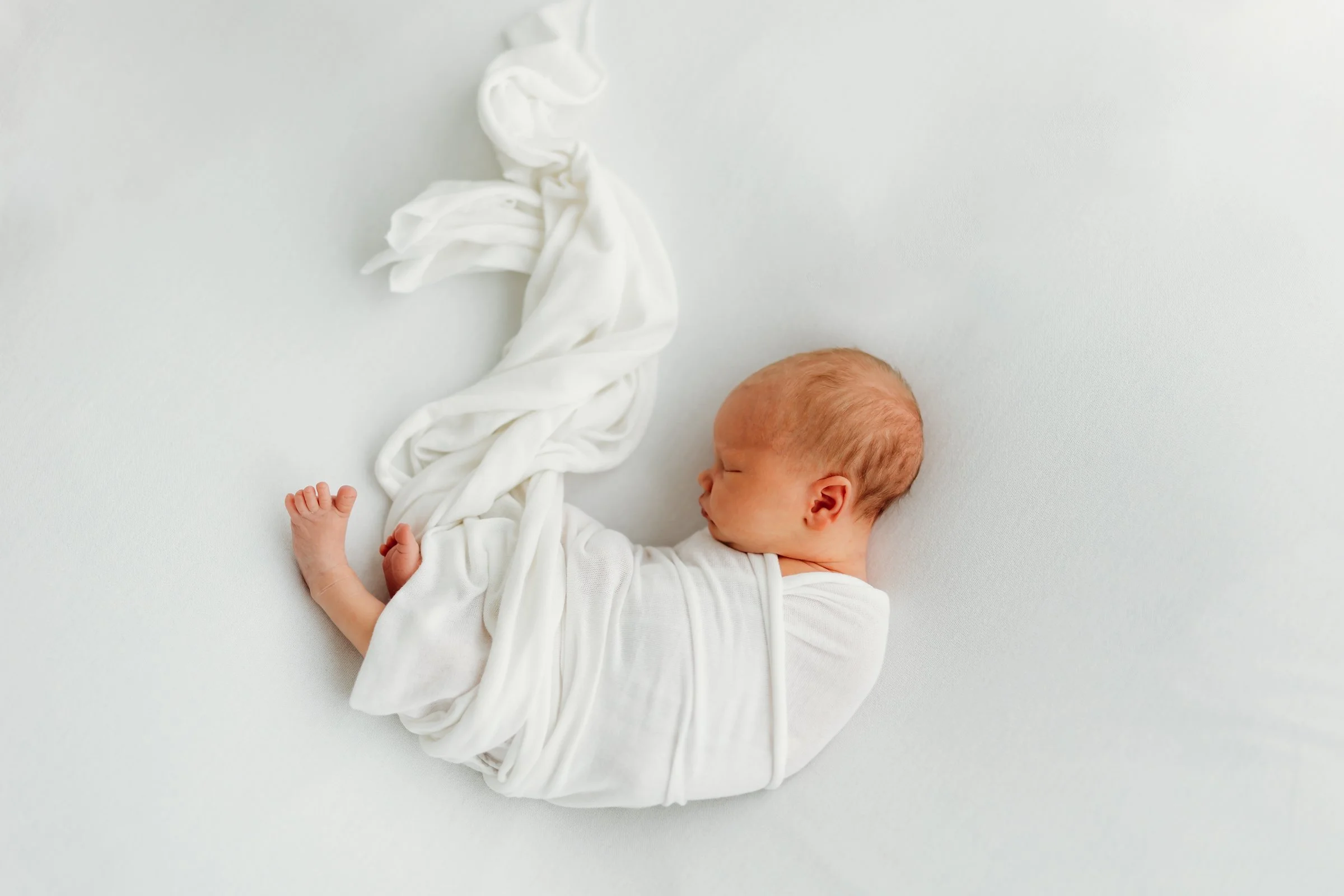 Newborn baby sleeping on a white blanket wrapped in a white cloth