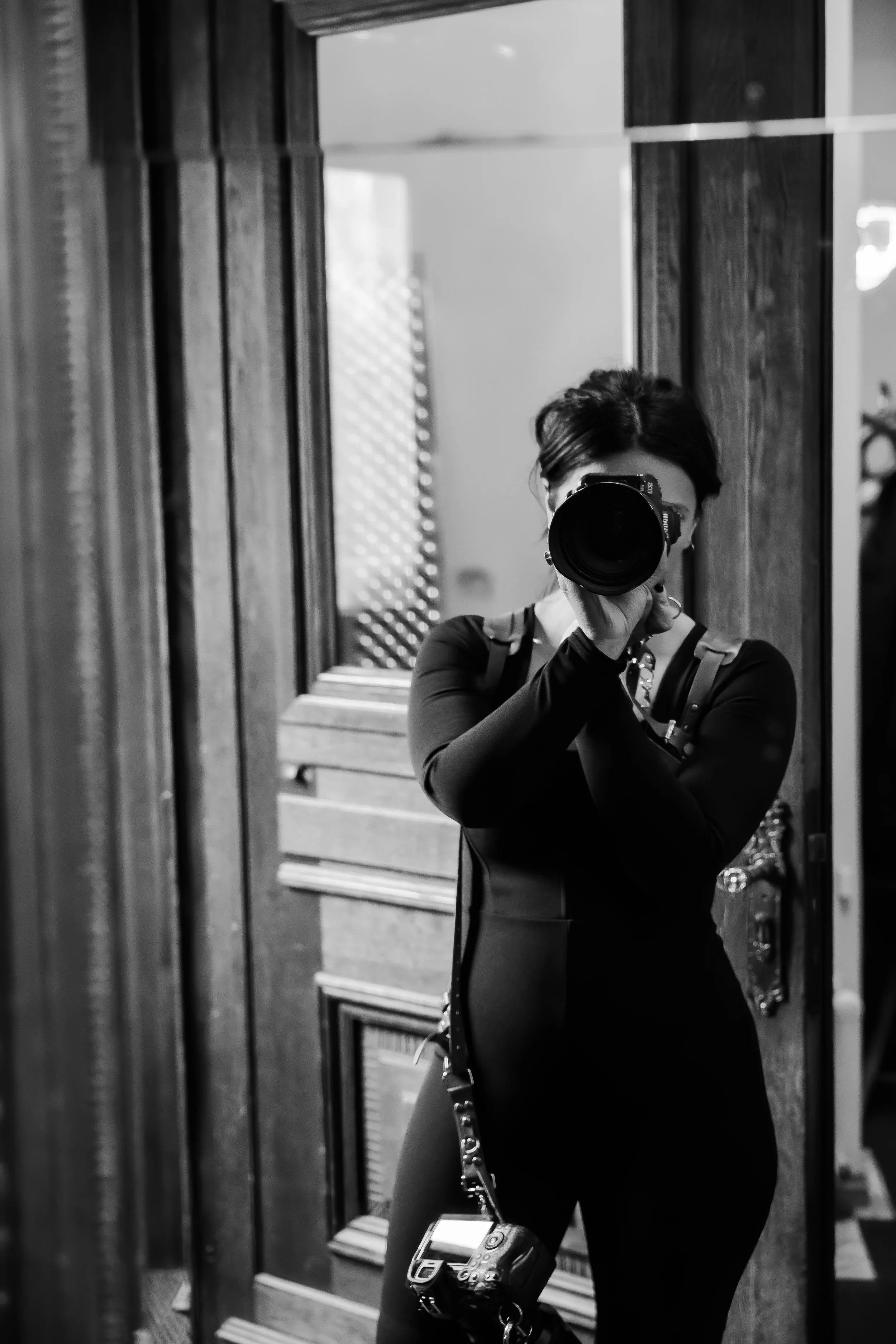 Person taking a photo of herself in a mirror with a camera, reflected in a wooden framed mirror, in black and white.
