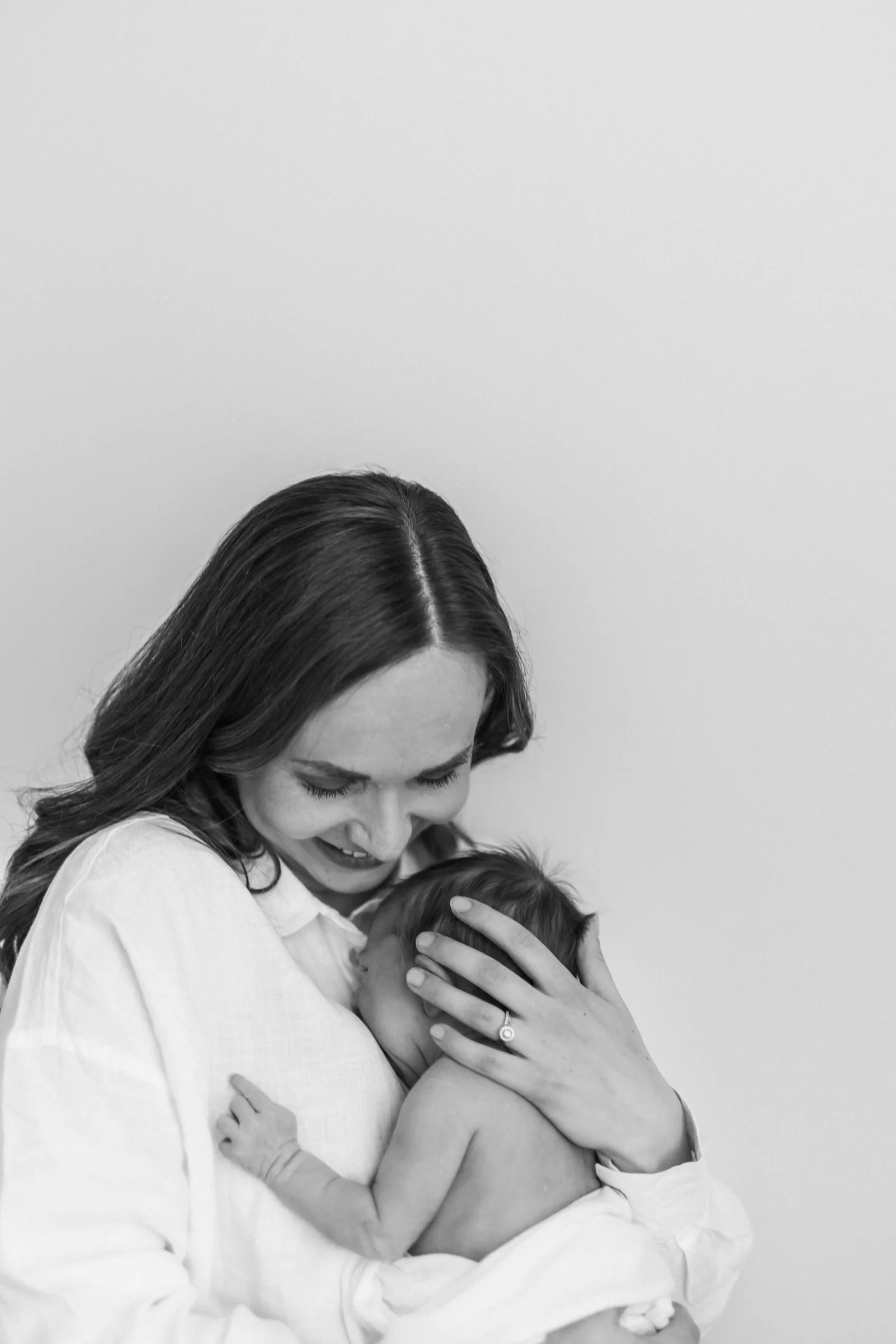 Black and white photo of a woman holding a baby close to her chest in an intimate moment.