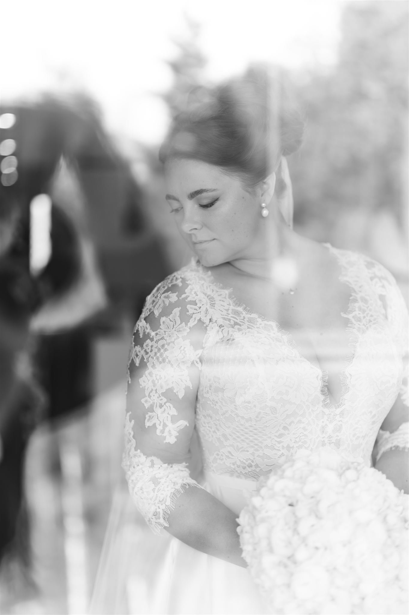 A bride in a lace wedding dress holding a bouquet of flowers, with her eyes closed and head slightly bowed.