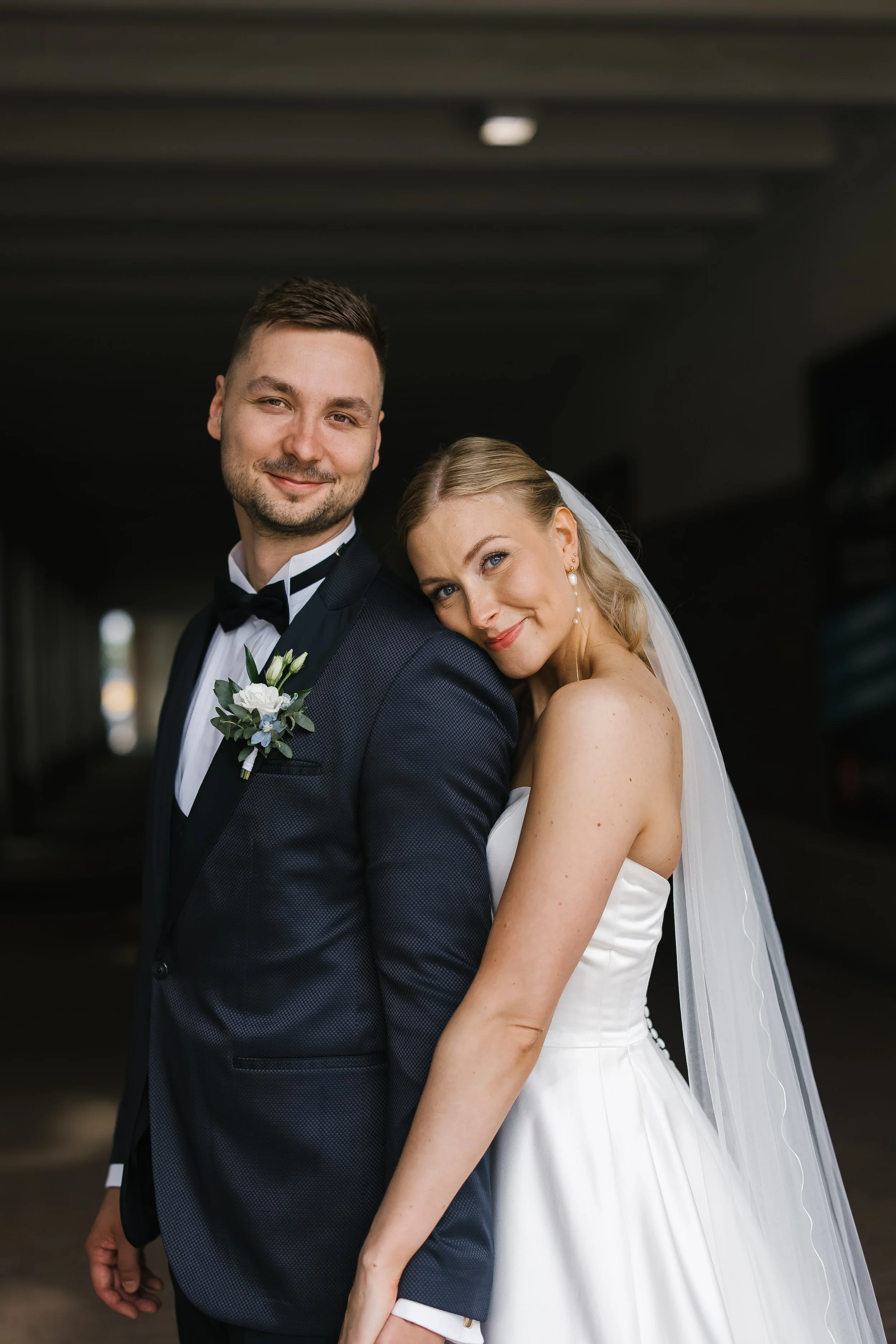 A bride and groom in wedding attire smiling together for a portrait.