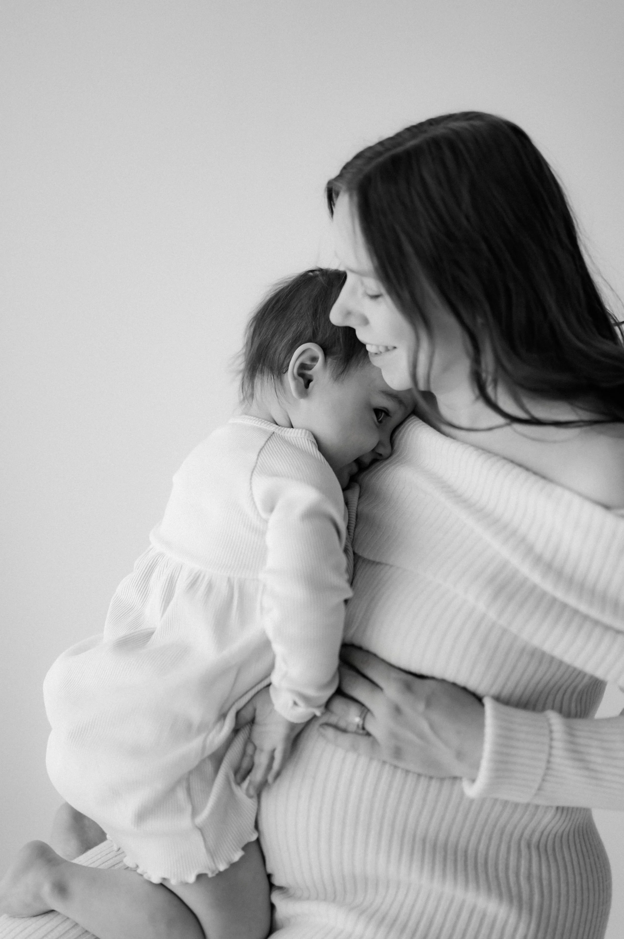A woman with dark hair holding a young girl close, both smiling and leaning their foreheads together, in a tender moment.