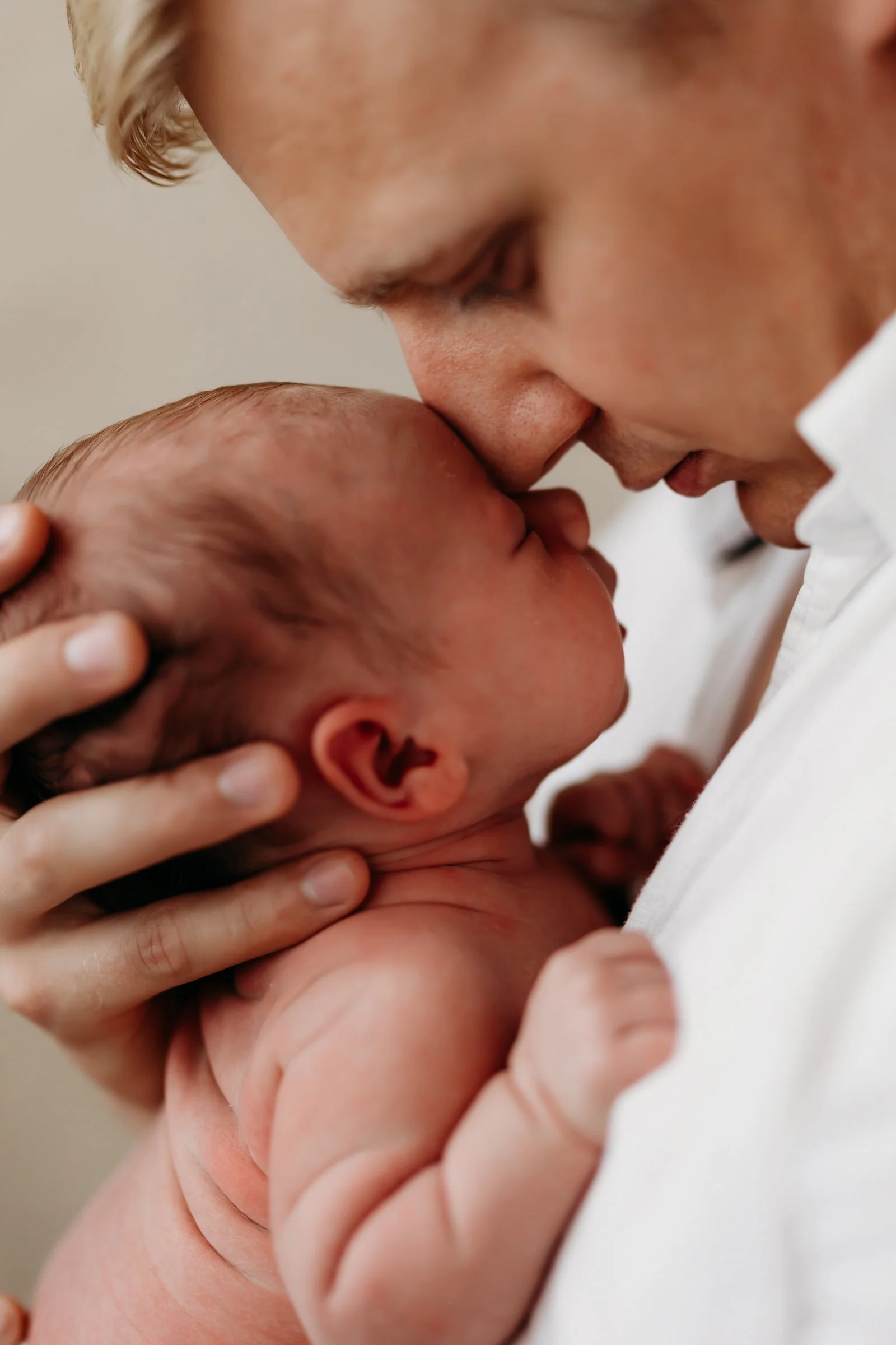 A person holding a newborn baby close, with their foreheads touching in a tender moment.