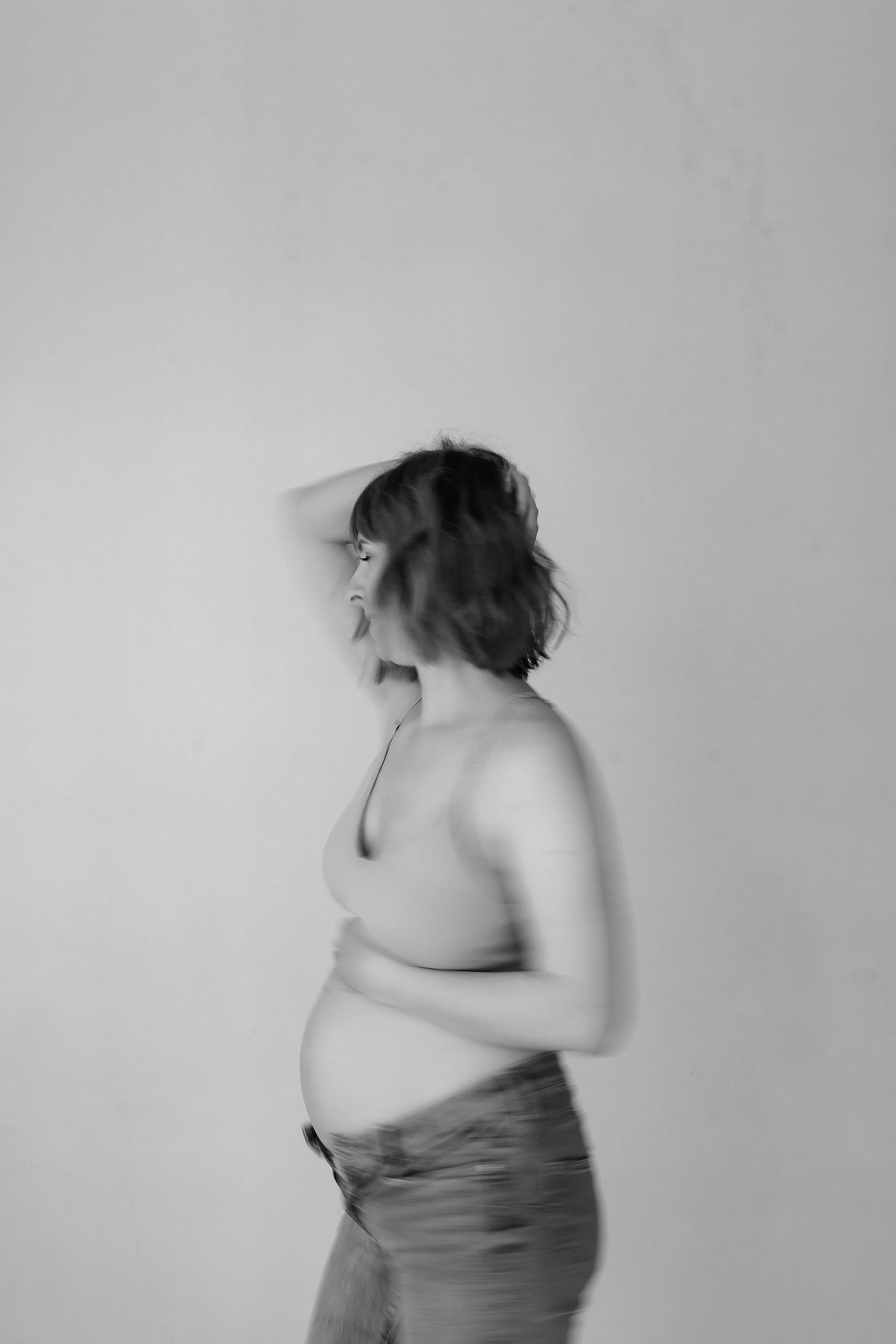Black and white photo of a pregnant woman standing against a plain wall, with her hand on her head and eyes closed.