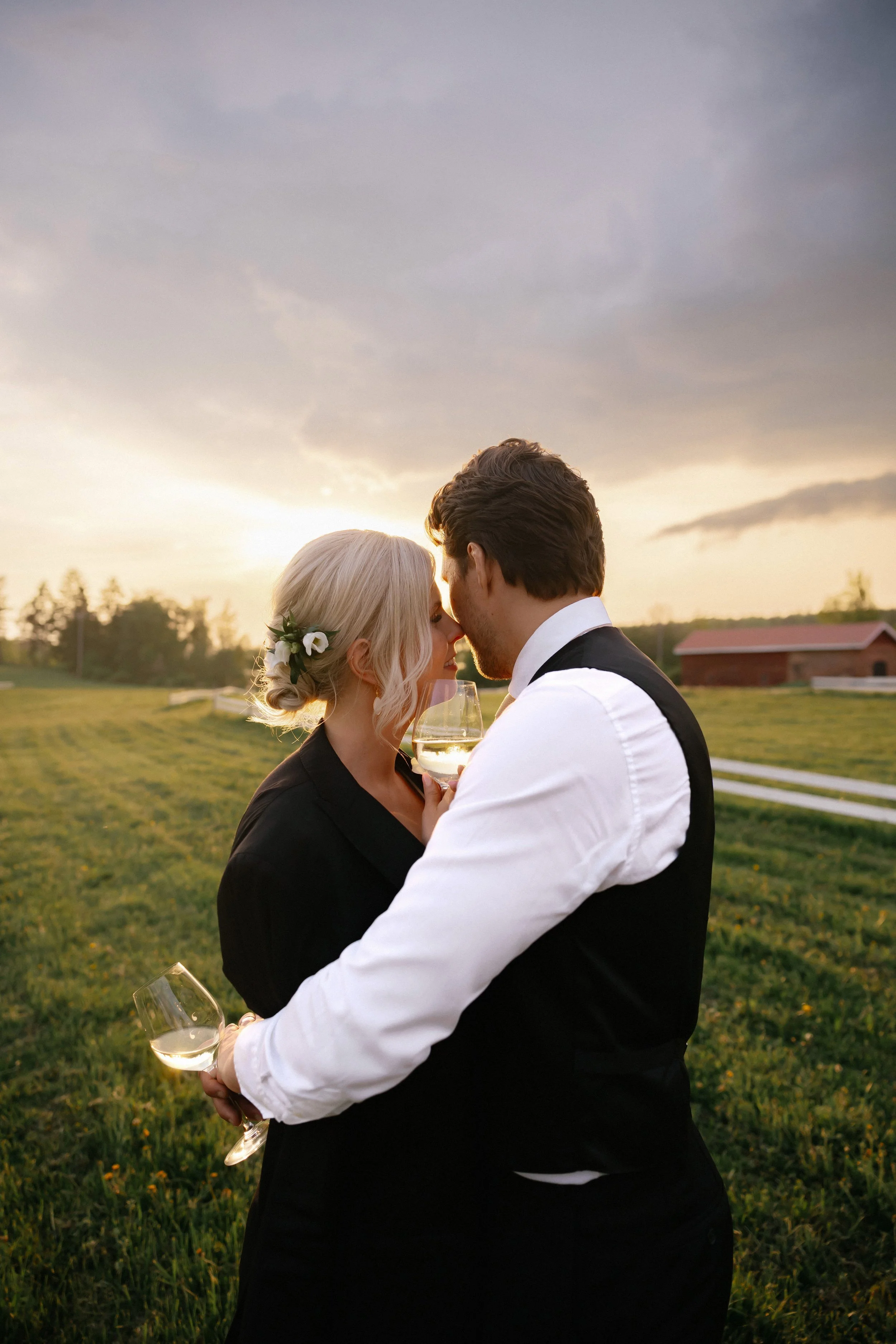 A couple with glasses of wine sharing an intimate moment at sunset outdoors.