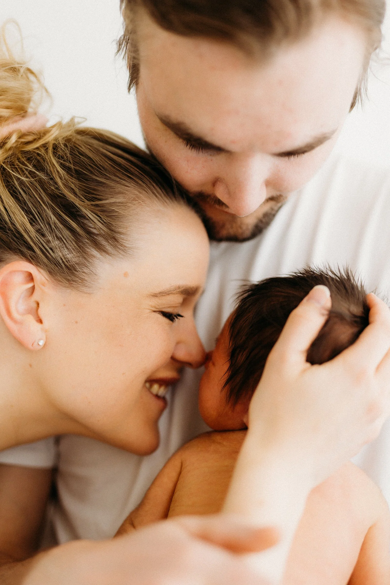 A family celebrating their newborn. The mother and father are holding and kissing their baby, smiling happily.