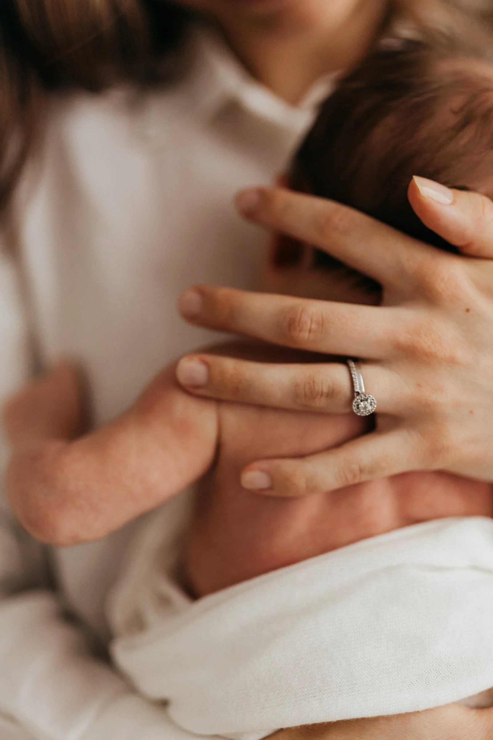 A woman holding a newborn baby close, with a ring on her finger.
