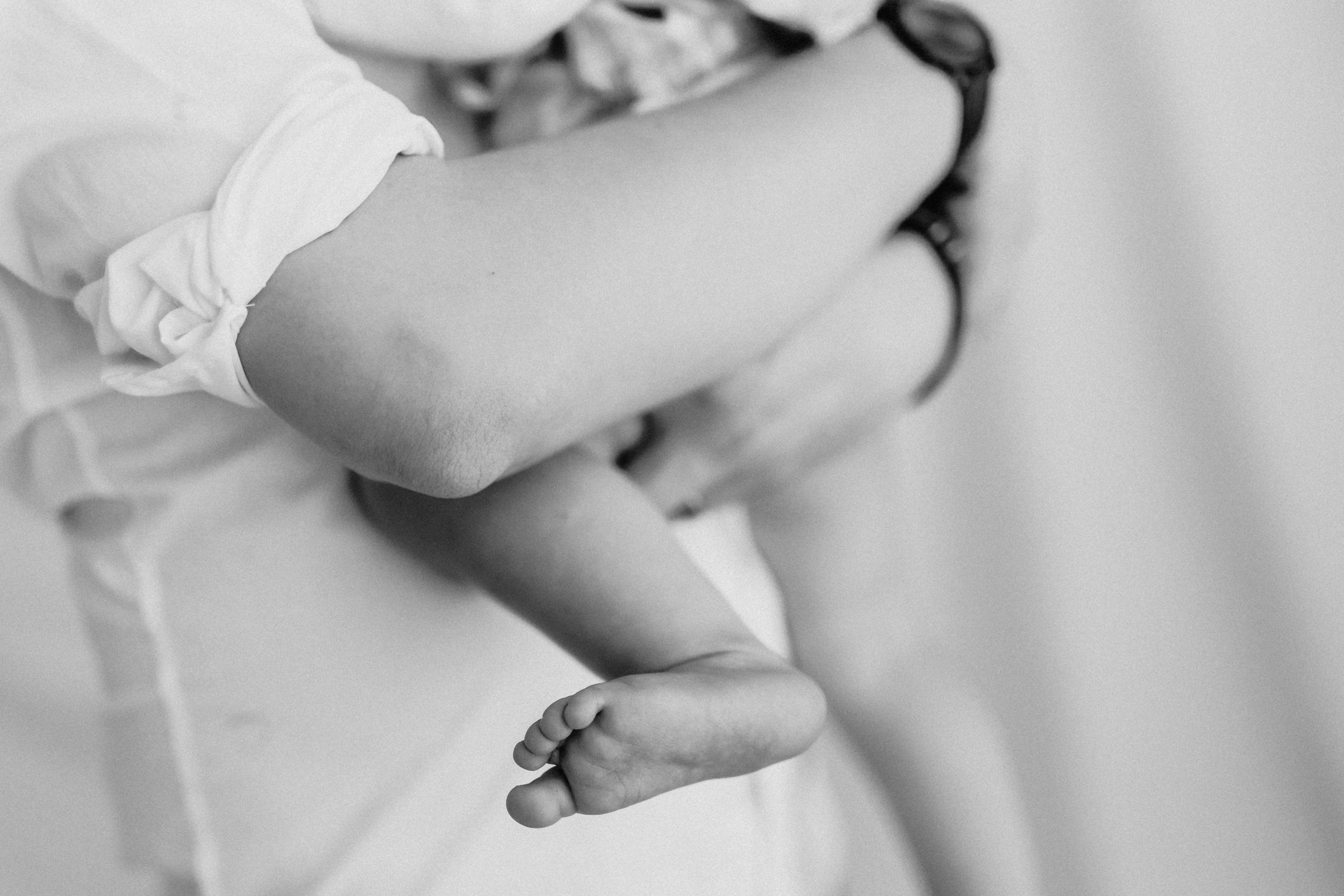 Close-up of a newborn baby's legs and feet, with one foot resting on a surface, in black and white.