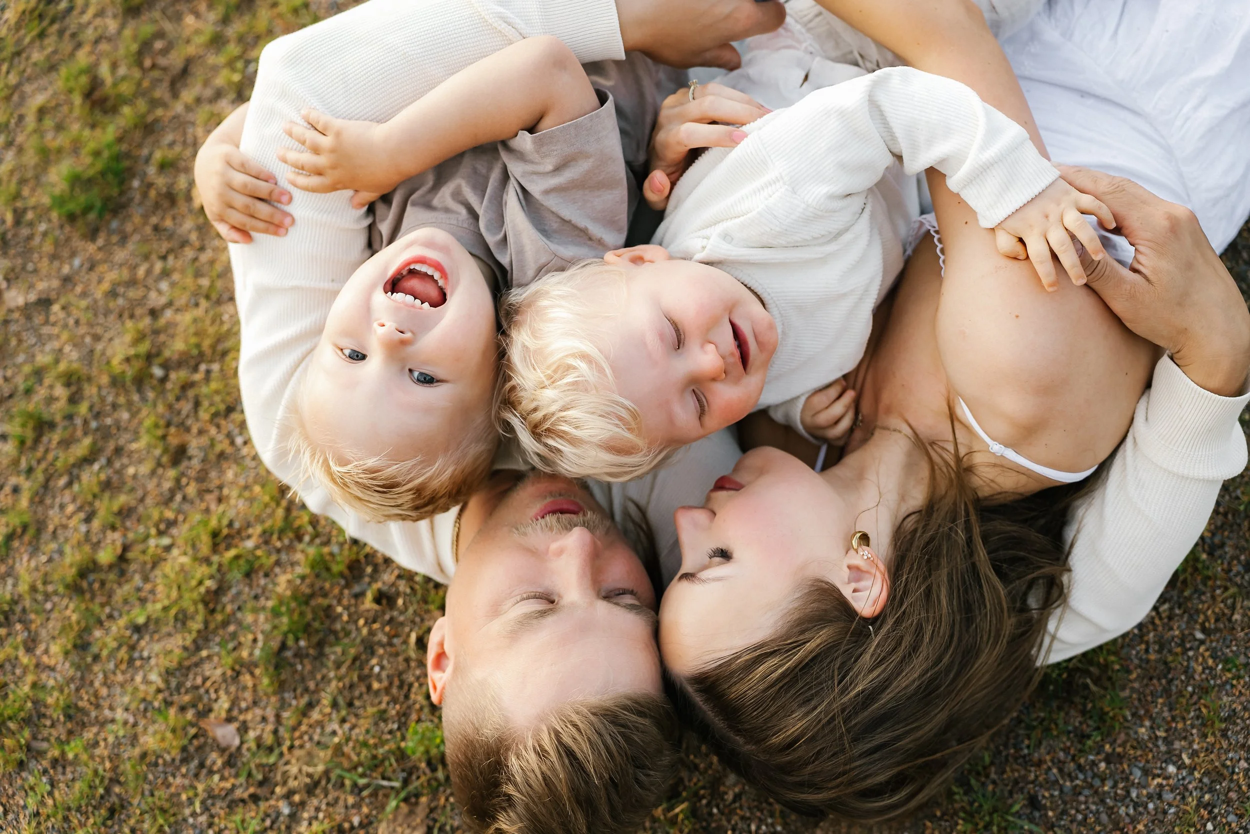A family of four lying on the ground outdoors, laughing and cuddling together.