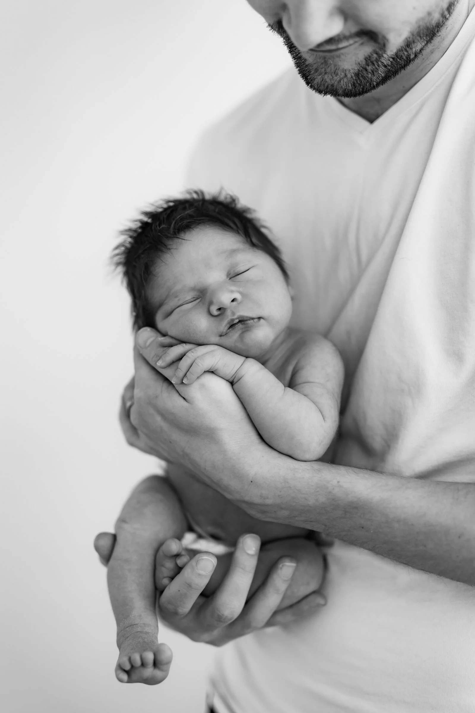 A man holding a sleeping newborn baby in his arms in black and white.