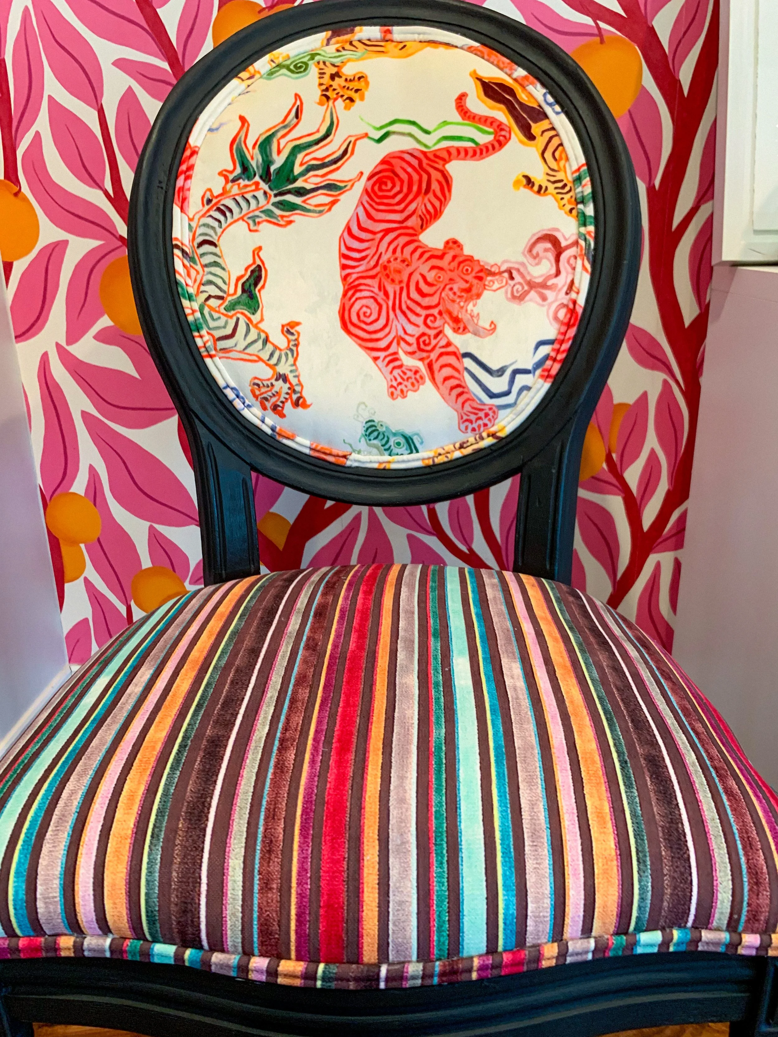 Vintage accent chair reupholstered in colorful striped velvet with tiger and dragon print back,set against bold pink and orange wallpaper in a maximalist design by Melissa B. Rodgers