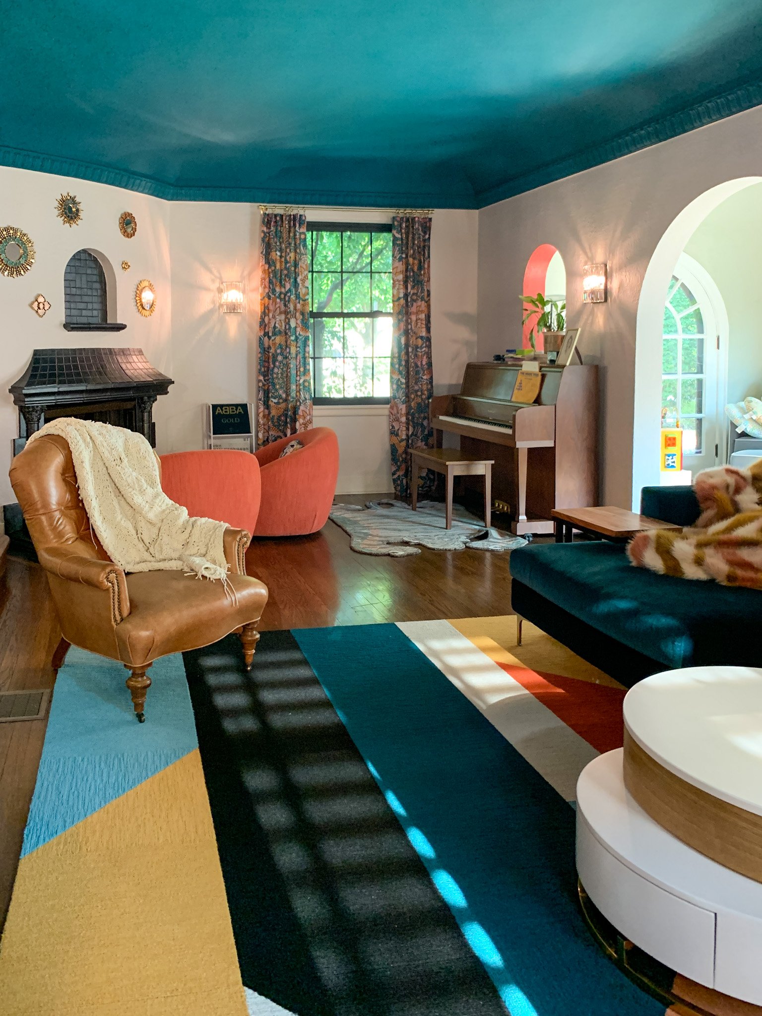 Colorful eclectic living room design with teal ceiling, geometric rug, and layered vintage furnishings created through E-Design services.