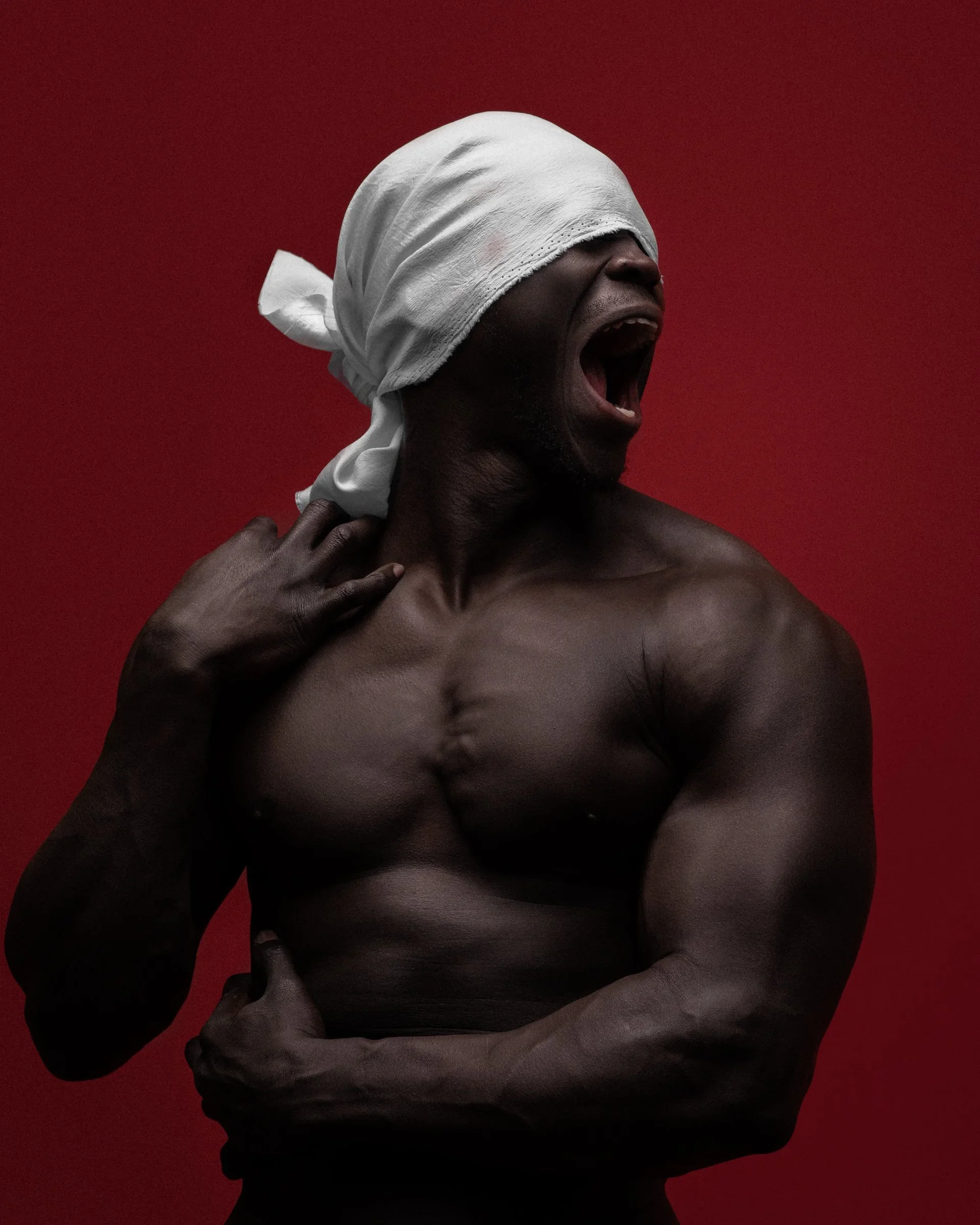 A shirtless man with dark skin wearing a white cloth tied around his head, shouting or yawning with a red background
