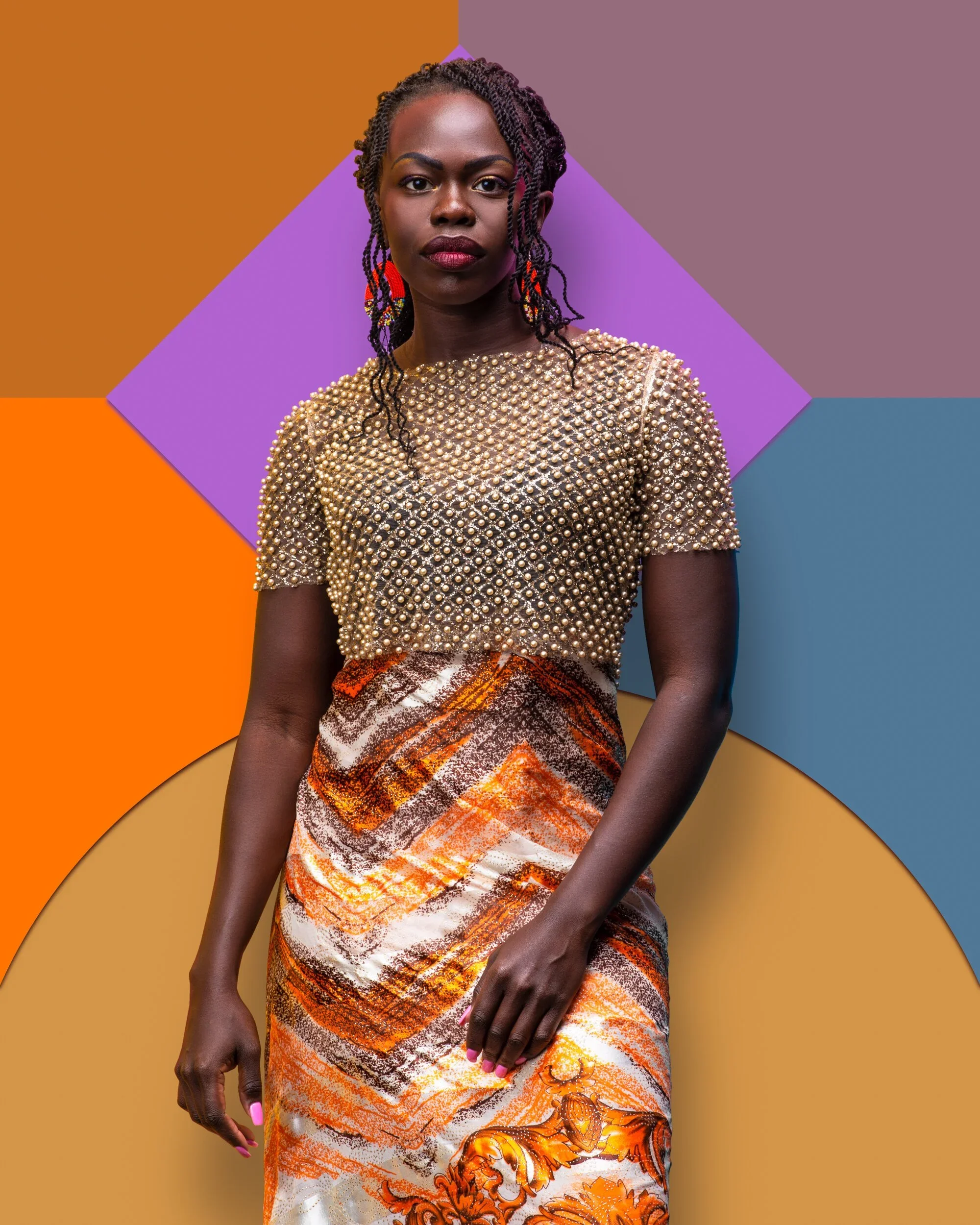 A woman wearing a gold beaded top and a patterned skirt stands against a colorful geometric background.