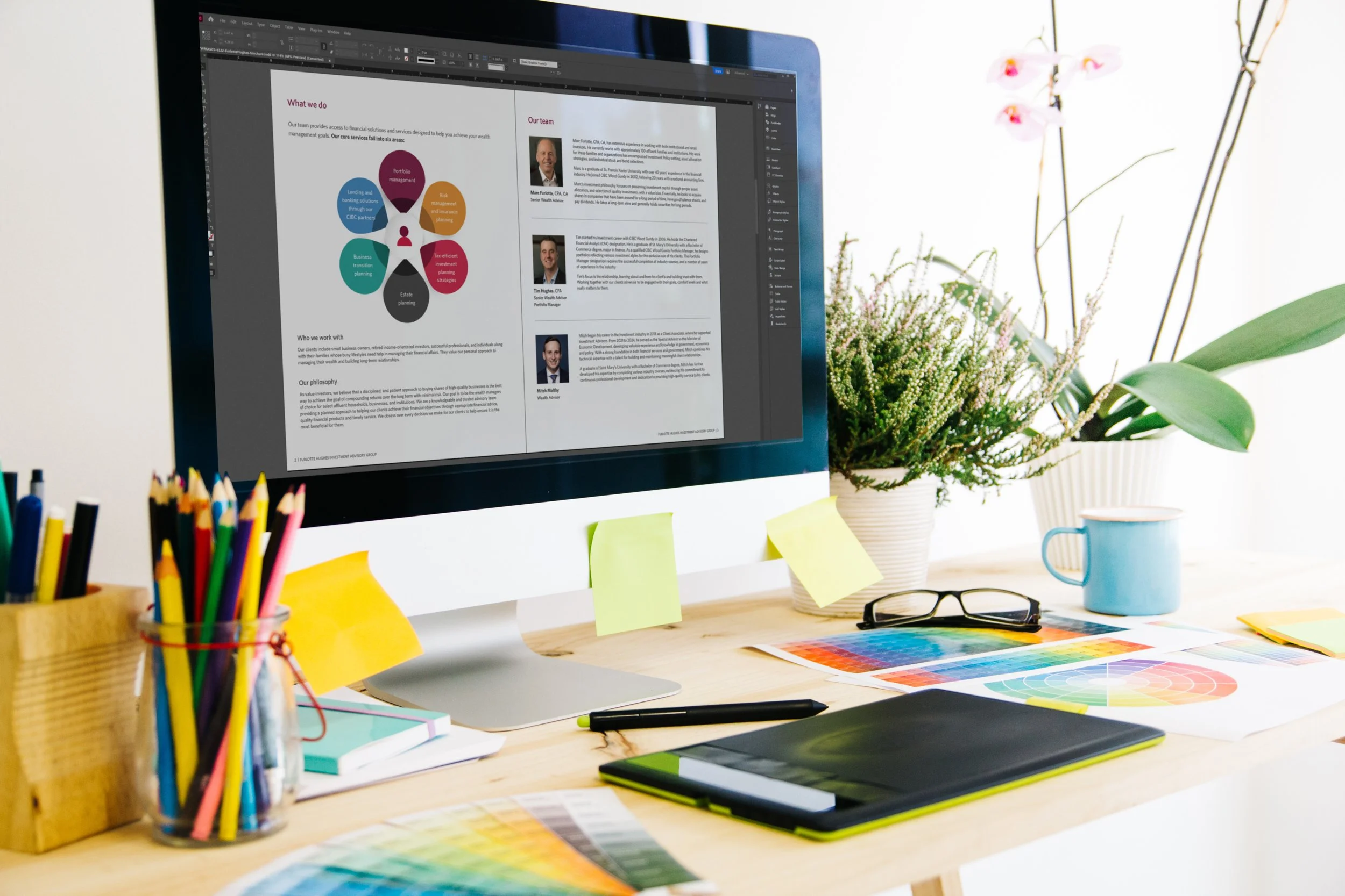 Open brochure layout displayed on a desktop computer in a creative workspace with a drawing tablet and design tools on the desk.