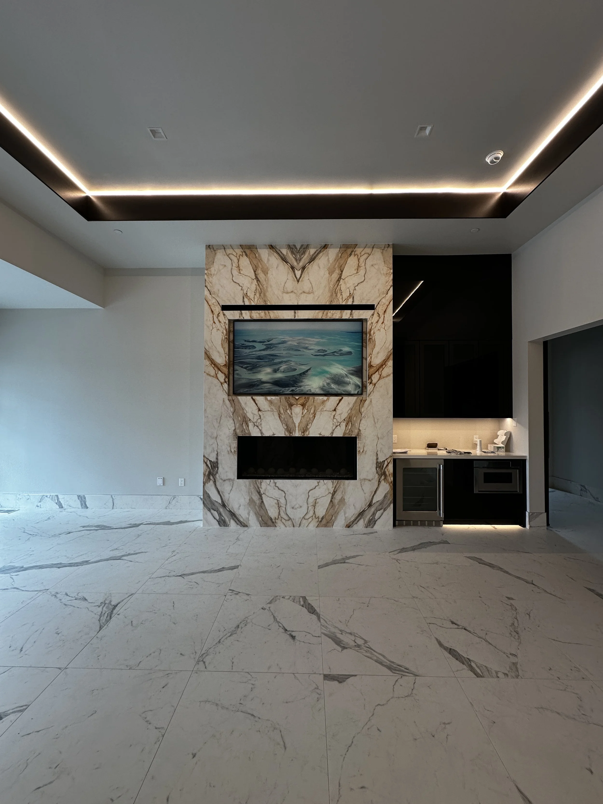 Modern living room with a marble fireplace and a mounted flat-screen TV above it, with a marble floor and a ceiling with recessed lighting.