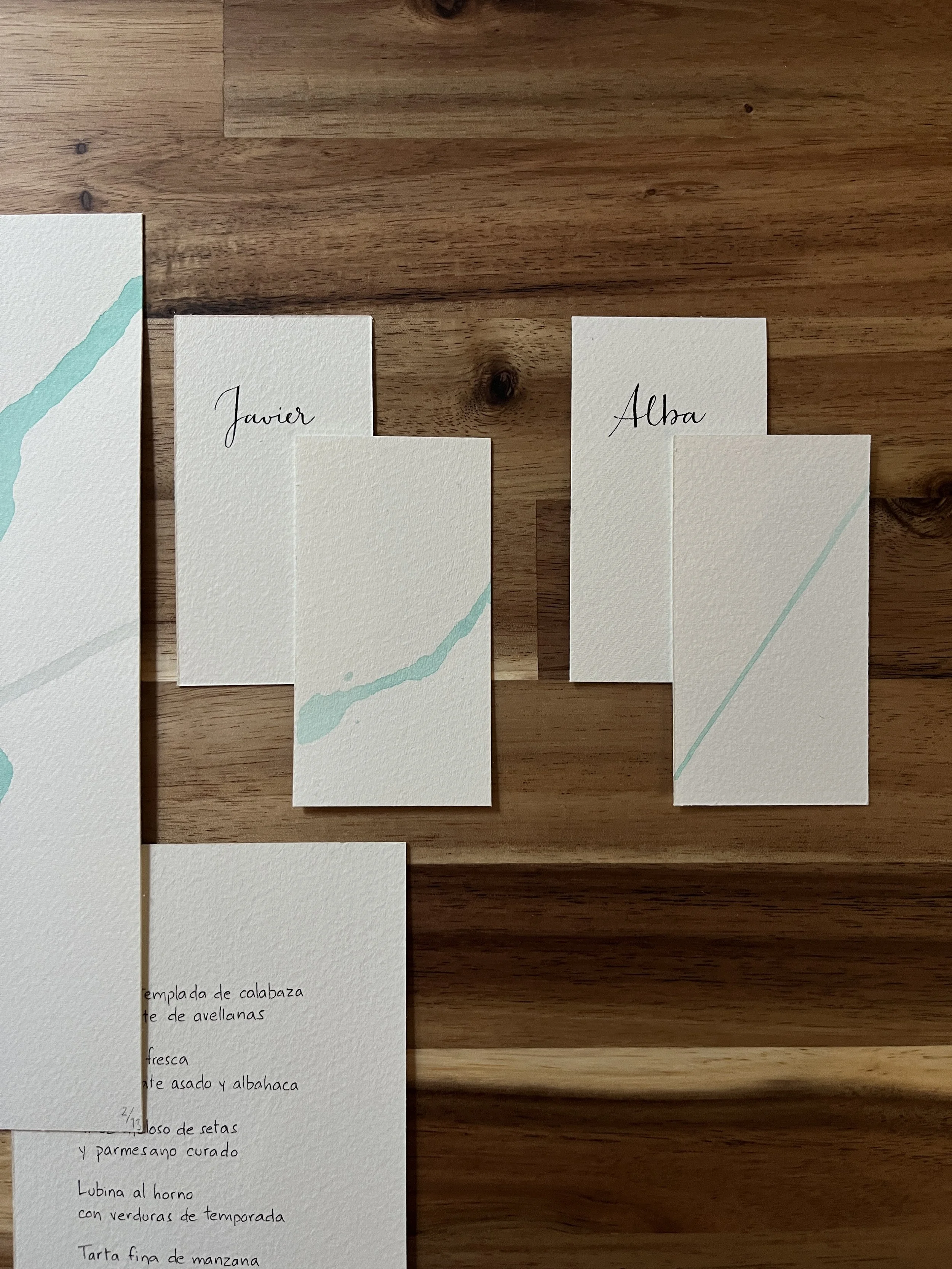 Diseño minimalista con trazo orgánico en marcasitios de boda Gesto Fluido escrita a mano.