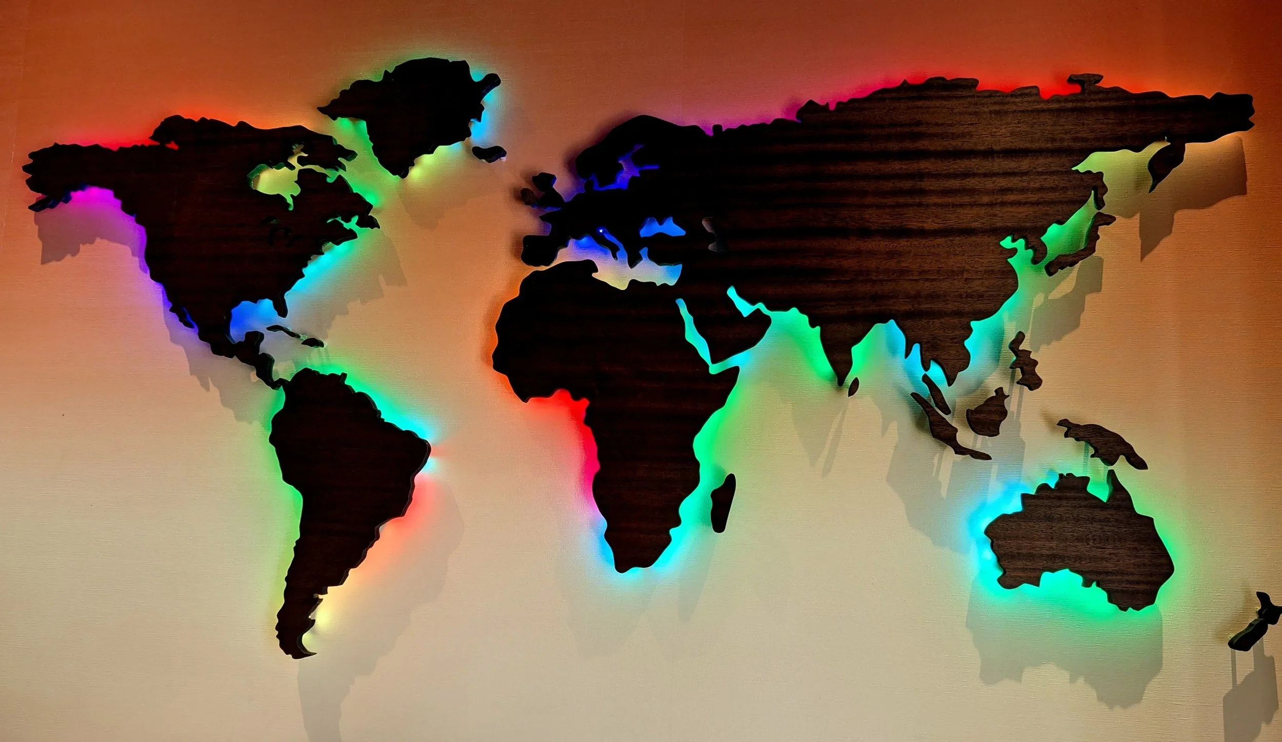 Wooden world map with colorful LED backlighting on a beige wall.