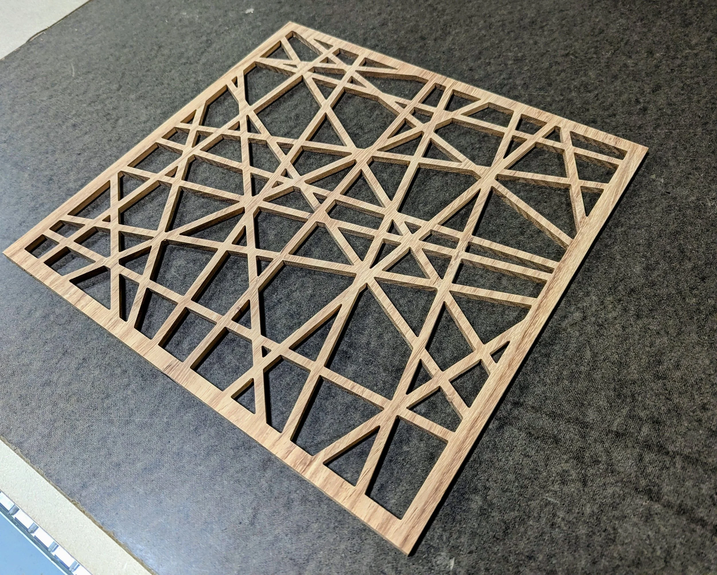 A rectangular wooden lattice with geometric cutouts, placed on a dark gray surface.