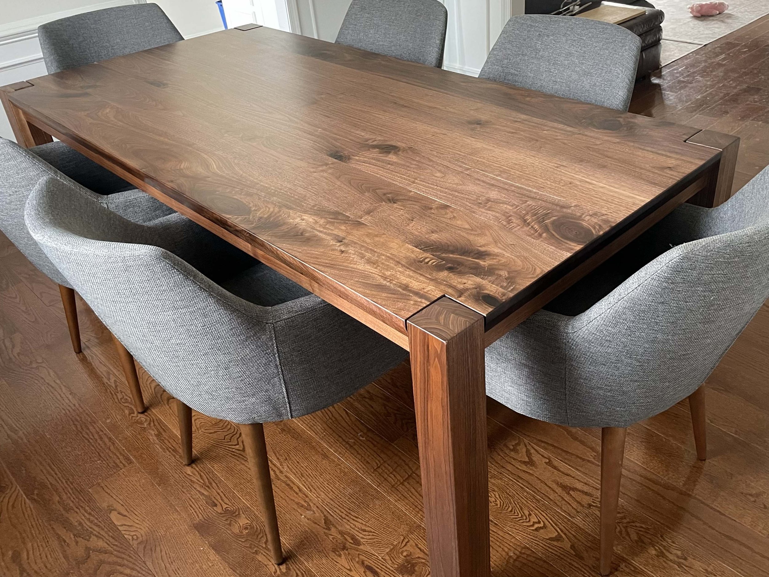 A rectangular wooden dining table with a polished surface, surrounded by six grey upholstered chairs on a wooden floor.
