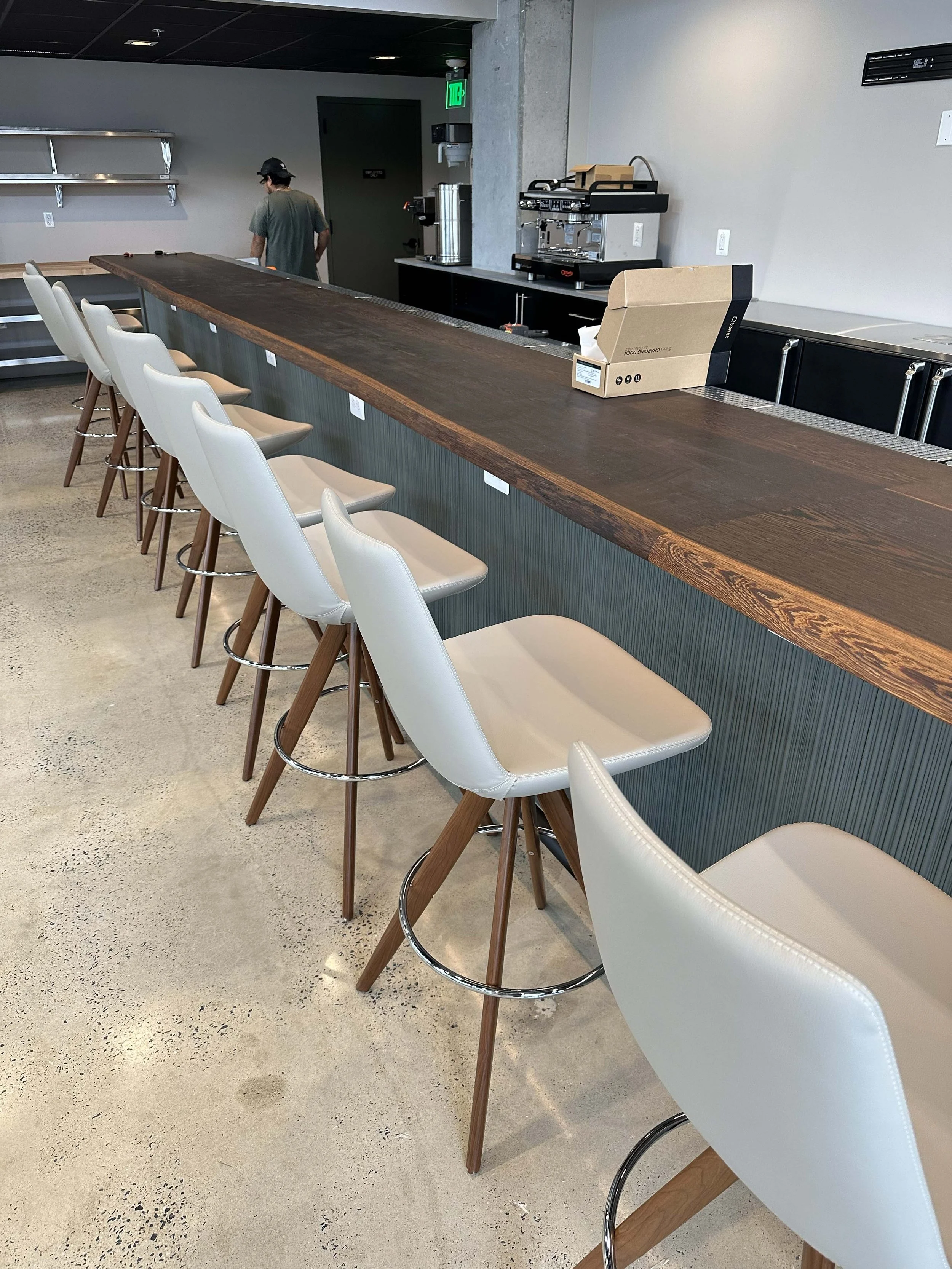 Empty bar counter with beige chairs, a large cardboard box, and brewing equipment in a modern cafe or bar setting.