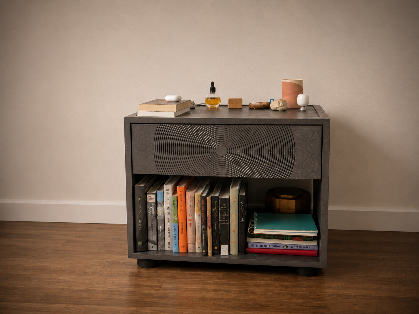 Black nightstand with a CNC-carved concentric-circle drawer front and open lower shelf for books, beside a bed