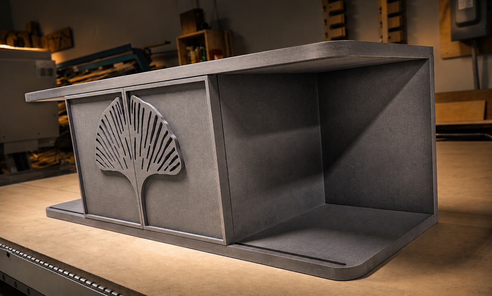 Gray credenza with a CNC-carved ginkgo leaf sliding door and open shelving, shown on the CNC table in the workshop