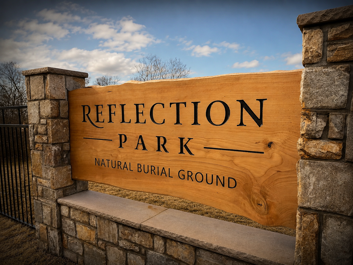 Spanish cedar entrance sign reading 'Reflection Park, Natural Burial Ground,' set between stone gate pillars