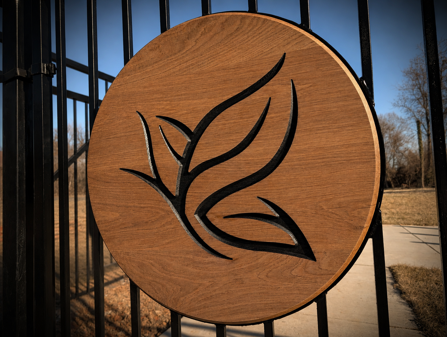 Round CNC-carved wood insert with a stylized leaf design, mounted on a black metal entrance gate