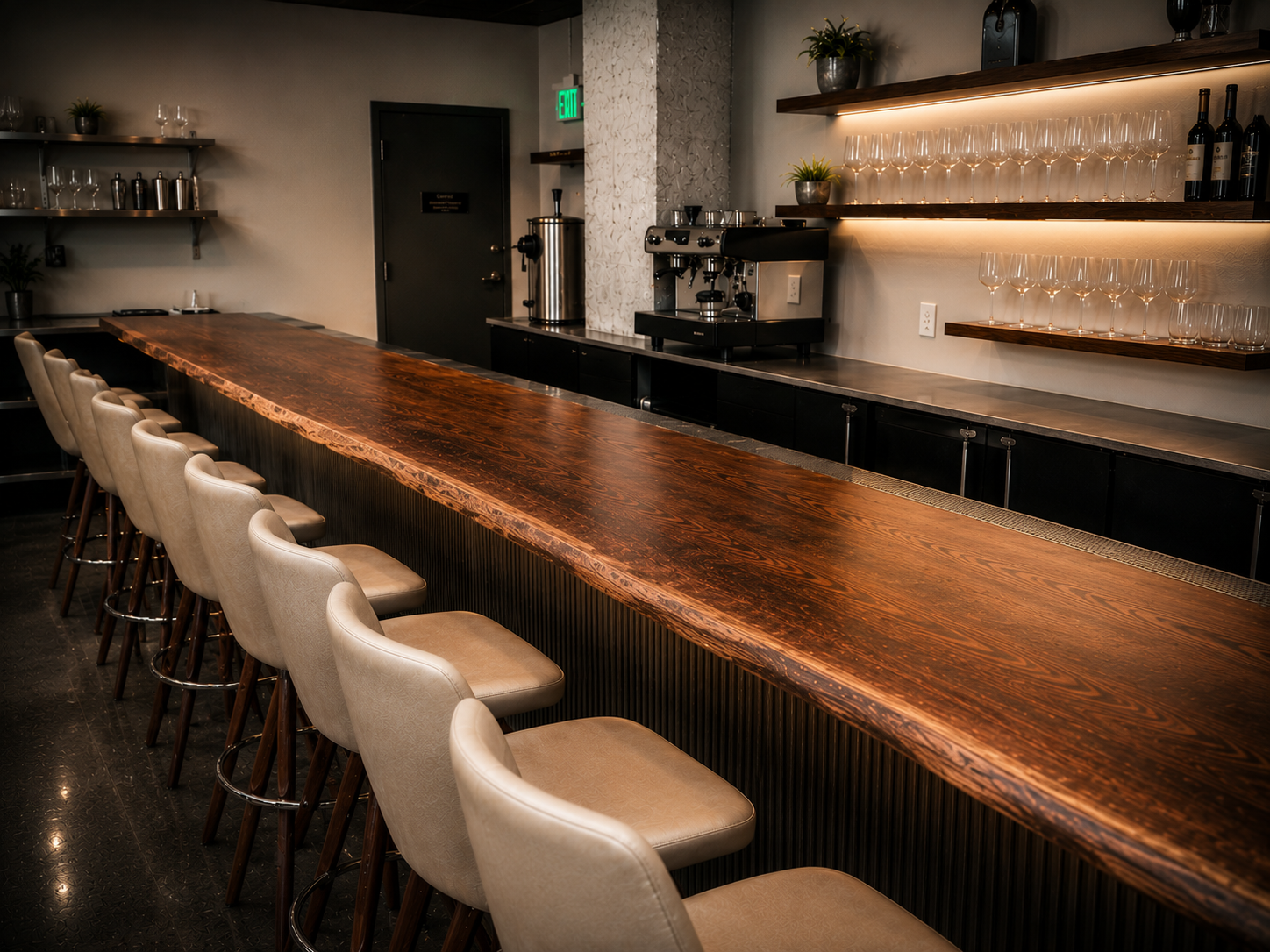 Long live-edge wood bar top with a fluted front panel and tan upholstered barstools, in a restaurant bar with backlit wine glass shelving