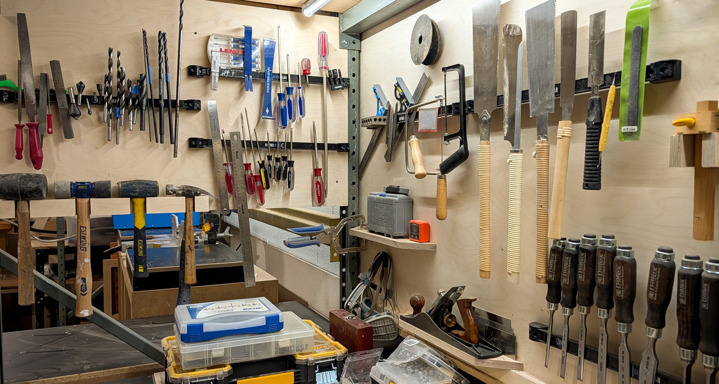A wooden wall with magnetic bars holds an array of hand saws, chisels, screwdrivers, drill bits and other woodworking tools