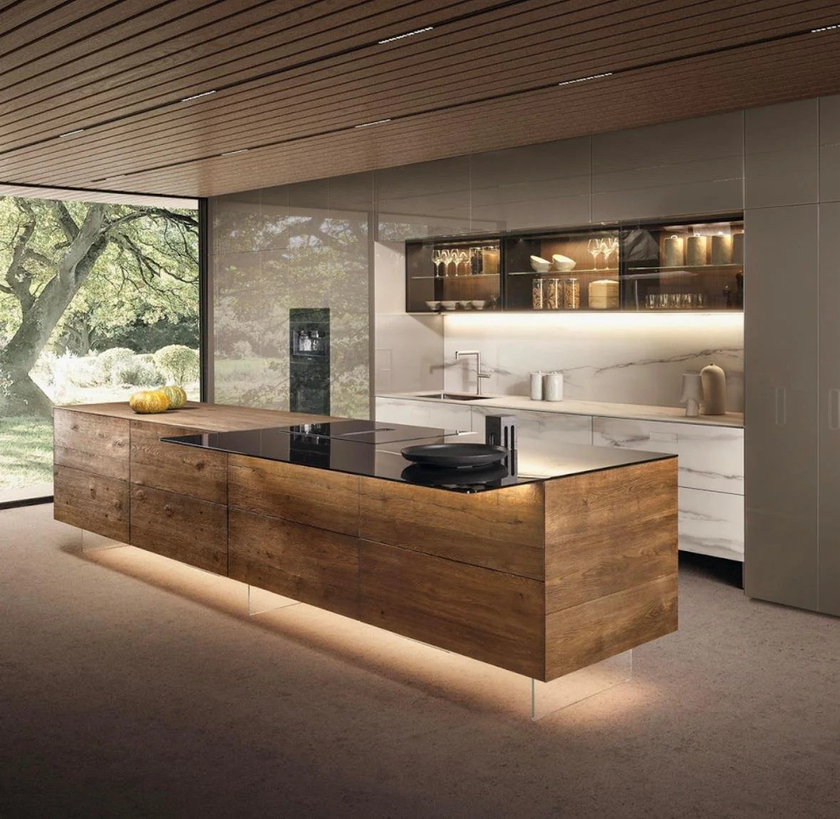 Cocina moderna con isla de madera, encimera negra, gabinetes de mármol blanco y estanterías abiertas con vajilla y frascos, vista a un jardín con árboles.