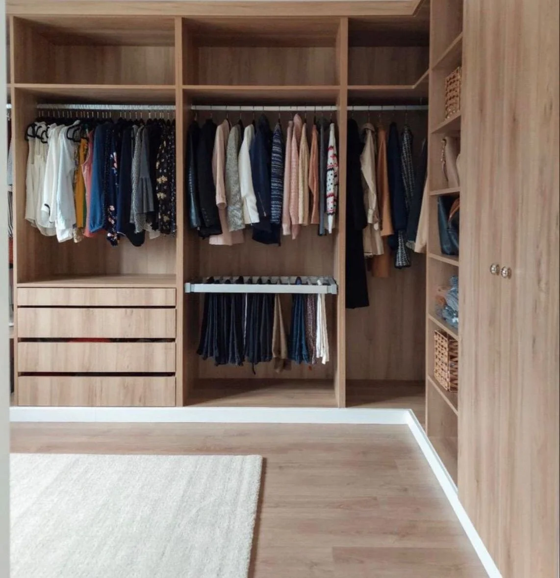 Vestidor con ropa organizada en perchas, algunos cajones y estantes de madera.