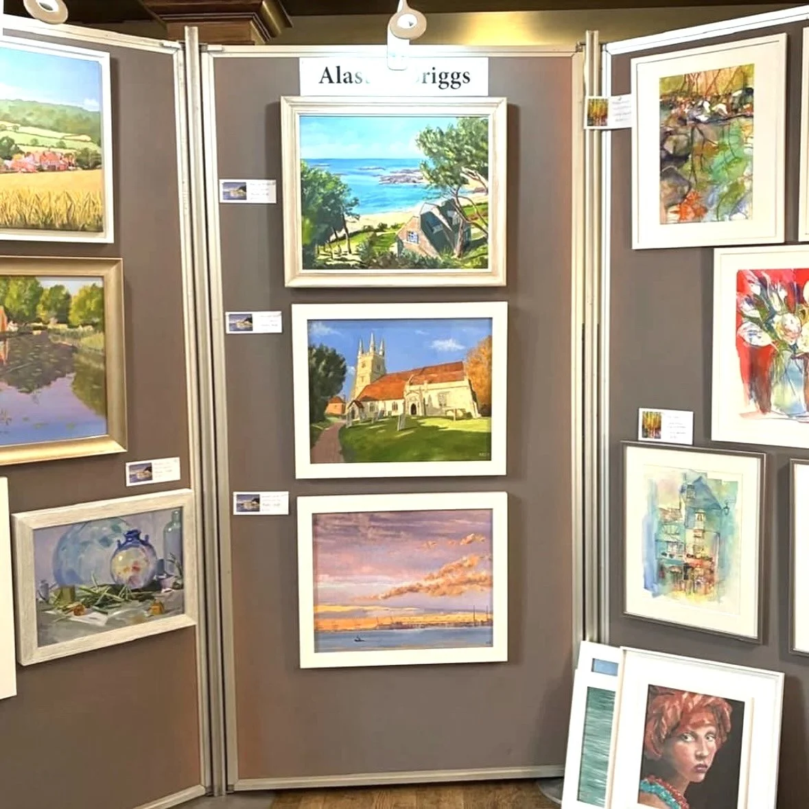 Collection of colorful landscape and portrait paintings displayed on an art exhibit wall.