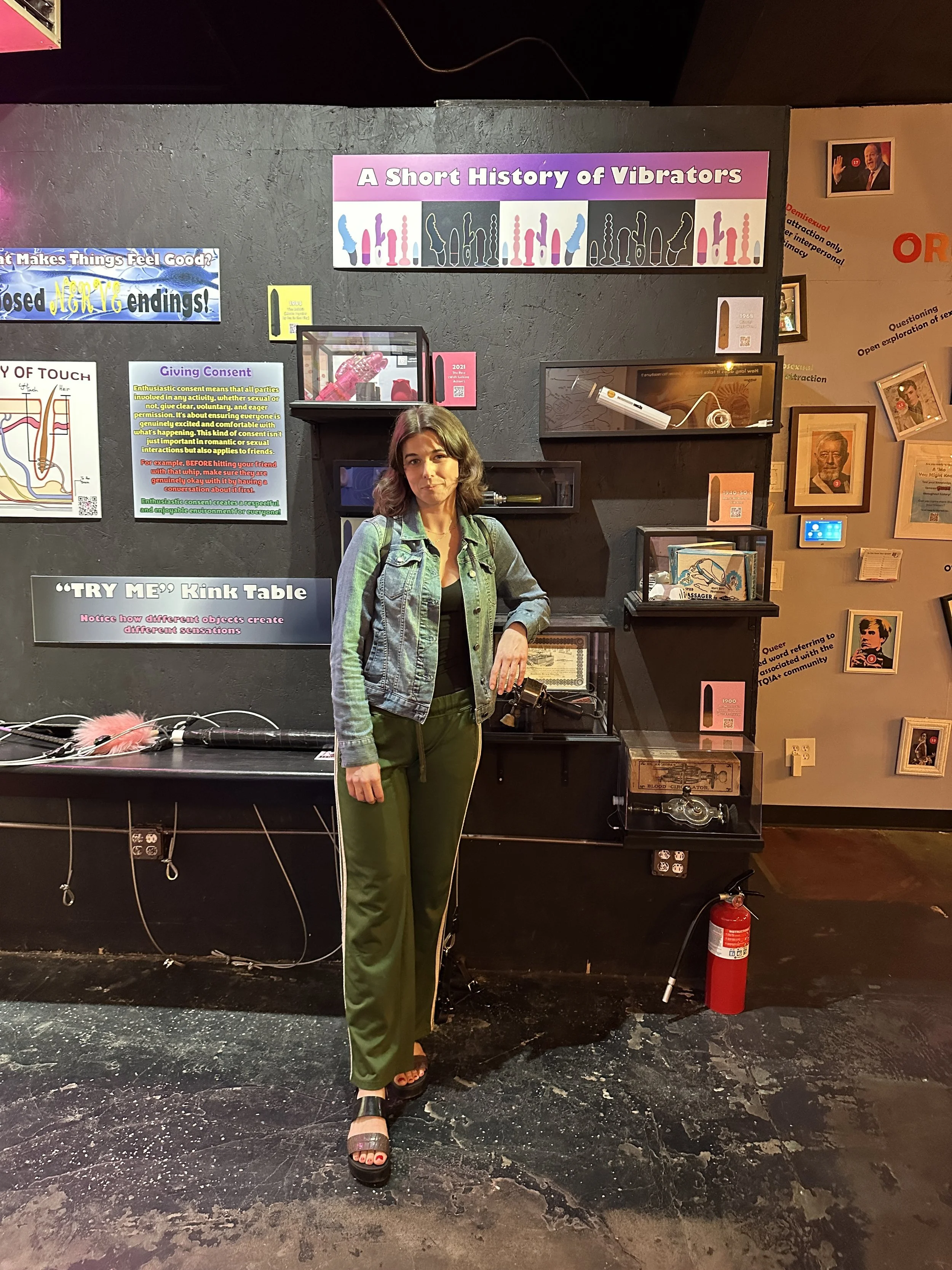 Victoria, a Fort Collins therapist and sexuality educator, standing in front of an intimacy history exhibit.