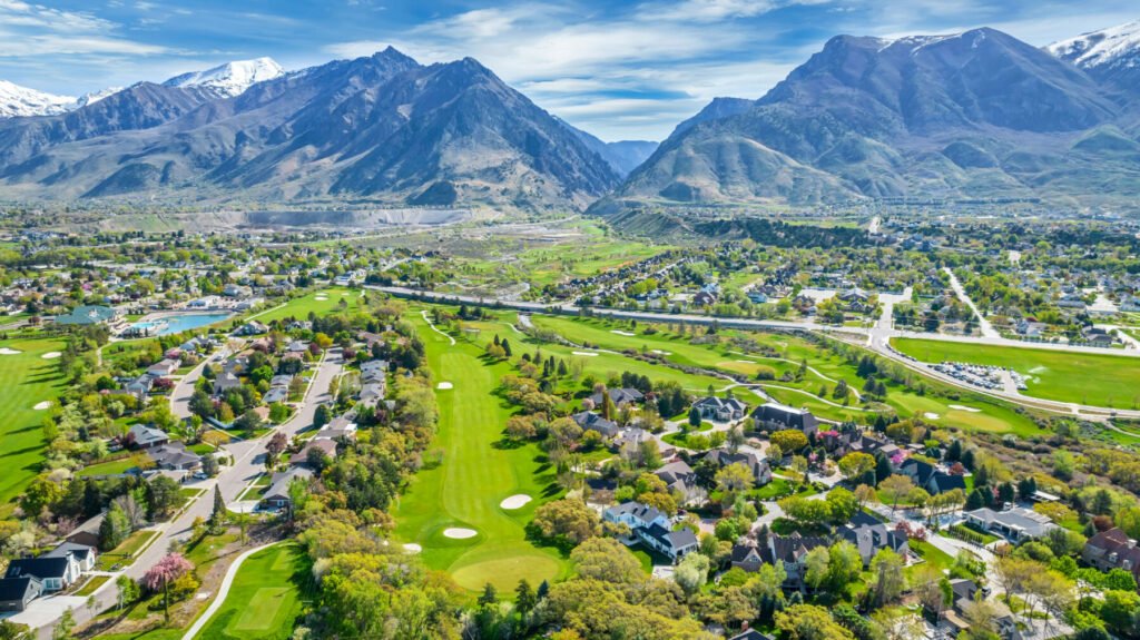 Aerial view of a residential neighborhood next to a golf course with a mountain range in the background.