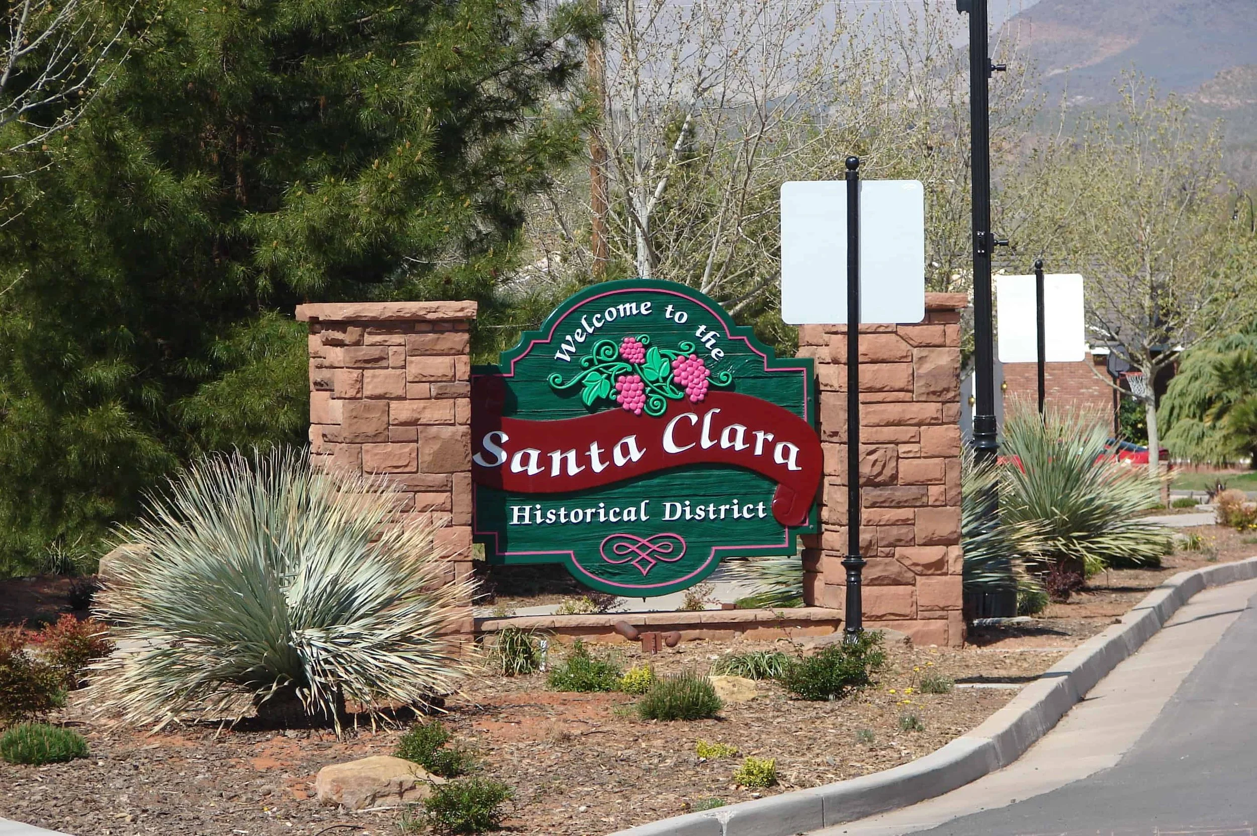 Welcome to the Santa Clara Historical District sign, with red brick columns, greenery, and a sidewalk.