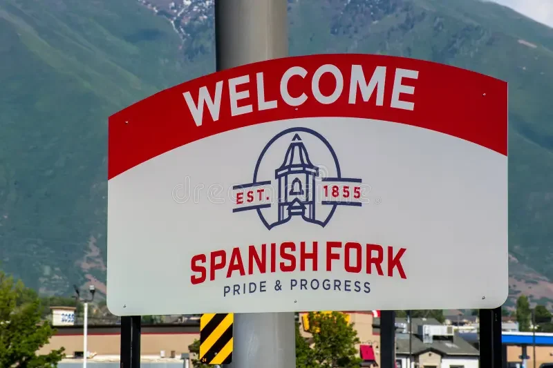 Welcome sign for Spanish Fork, Utah, featuring a church steeple and the text 'PRIDE & PROGRESS' with mountains in the background.