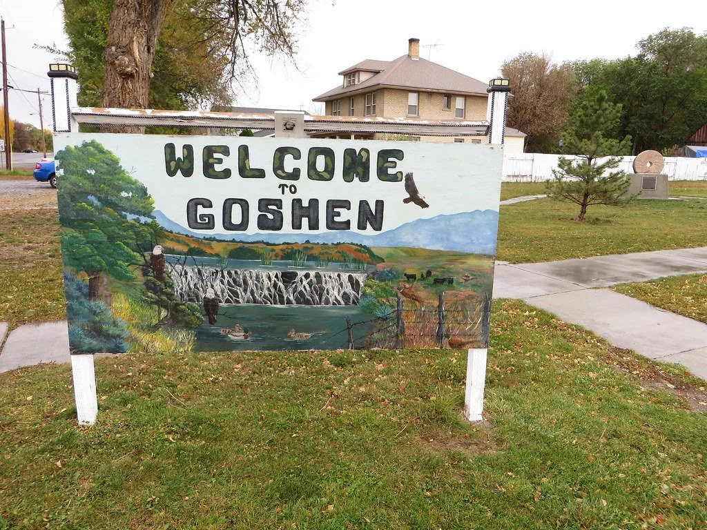 Colorful mural sign that reads 'Welcome to Goshen' with a painted landscape of a river, waterfall, trees, mountains, and birds.