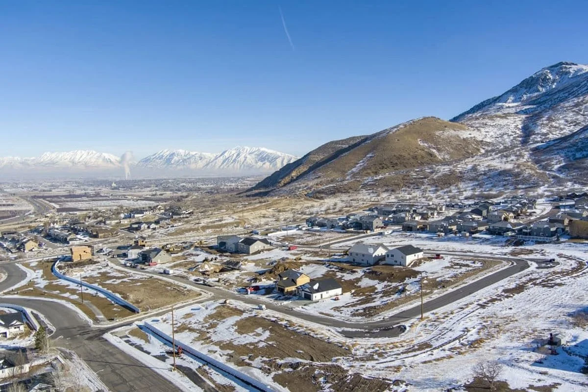 Snow-covered residential neighborhood at the base of a mountain range with clear blue sky.