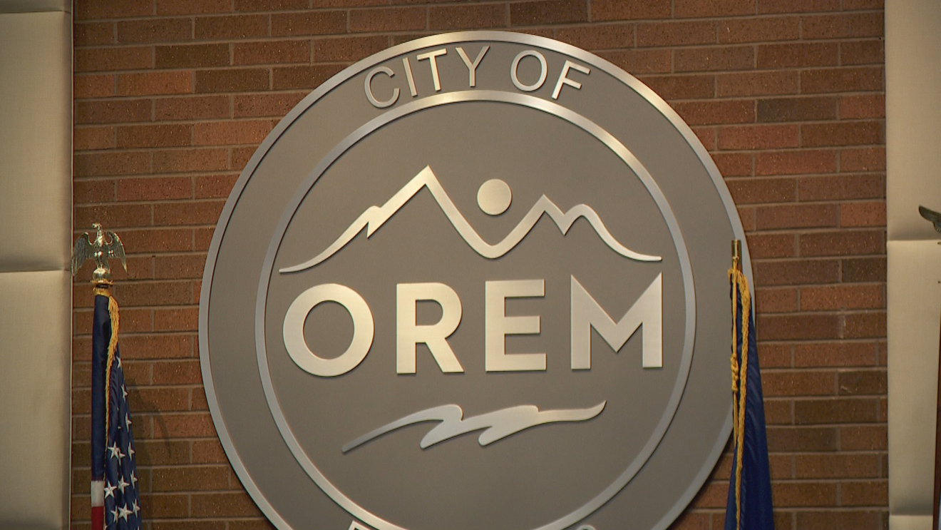 The city of Orem official emblem on a brick wall, with American flags on either side.