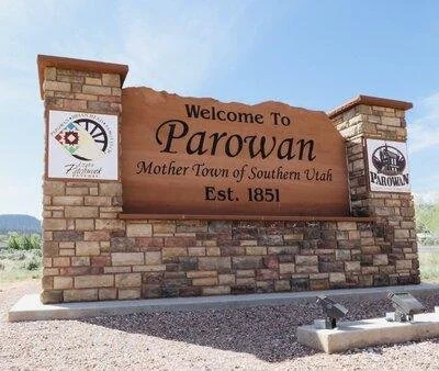Welcome sign for Parowan, Utah, with brick and stone structure, including a wooden sign that reads "Welcome To Parowan Mother Town of Southern Utah Est. 1851" and nearby signage.
