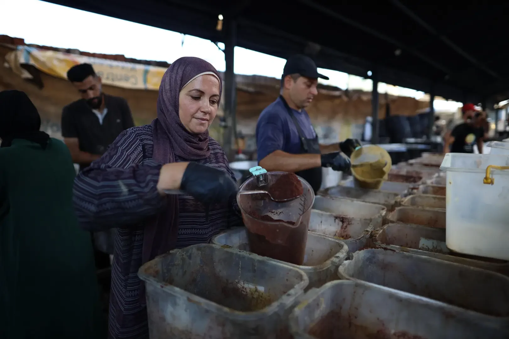 People working at a food stall or kitchen, preparing and pouring sauces or liquids into containers.