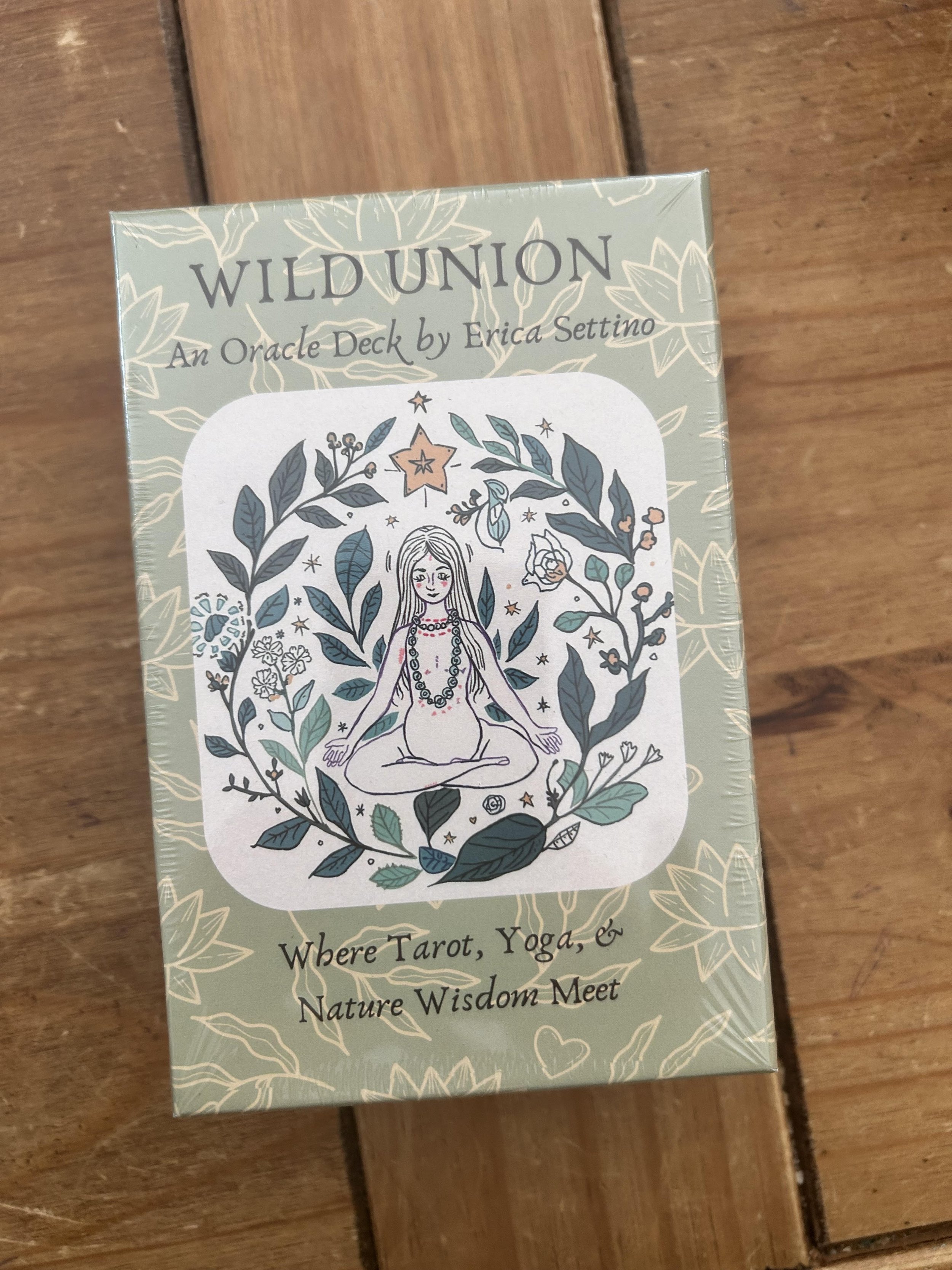 A deck of Wild Union tarot cards with an illustration of a meditating woman surrounded by leaves and stars on the cover.
