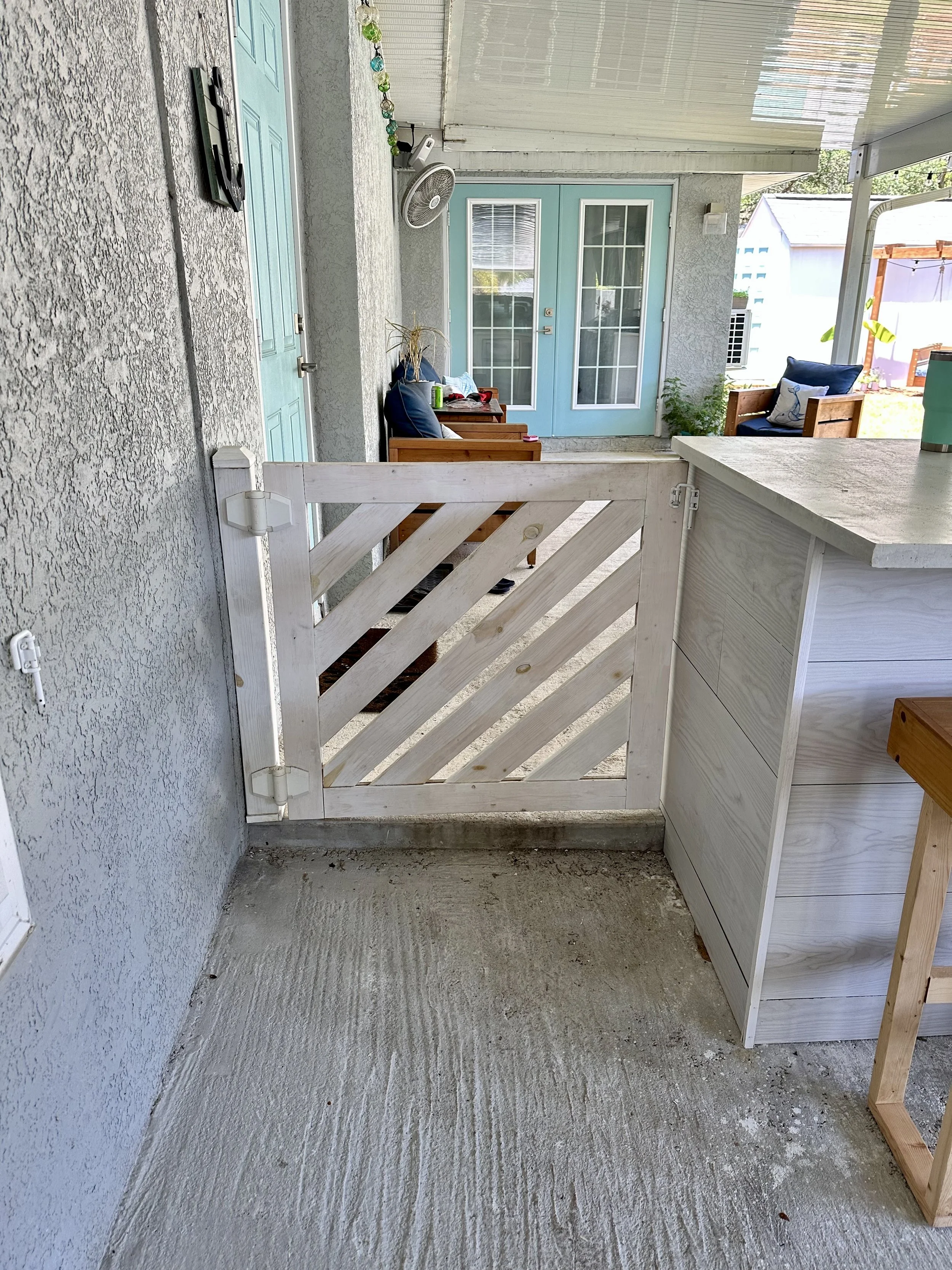 CUSTOM WOOD GATE, Gulfport, FL | Built to fit seamlessly into an outdoor kitchen, sectioning off the carport from the patio while keeping the space feeling open and cohesive. The diagonal slat design and whitewash finish give it a relaxed coastal cha