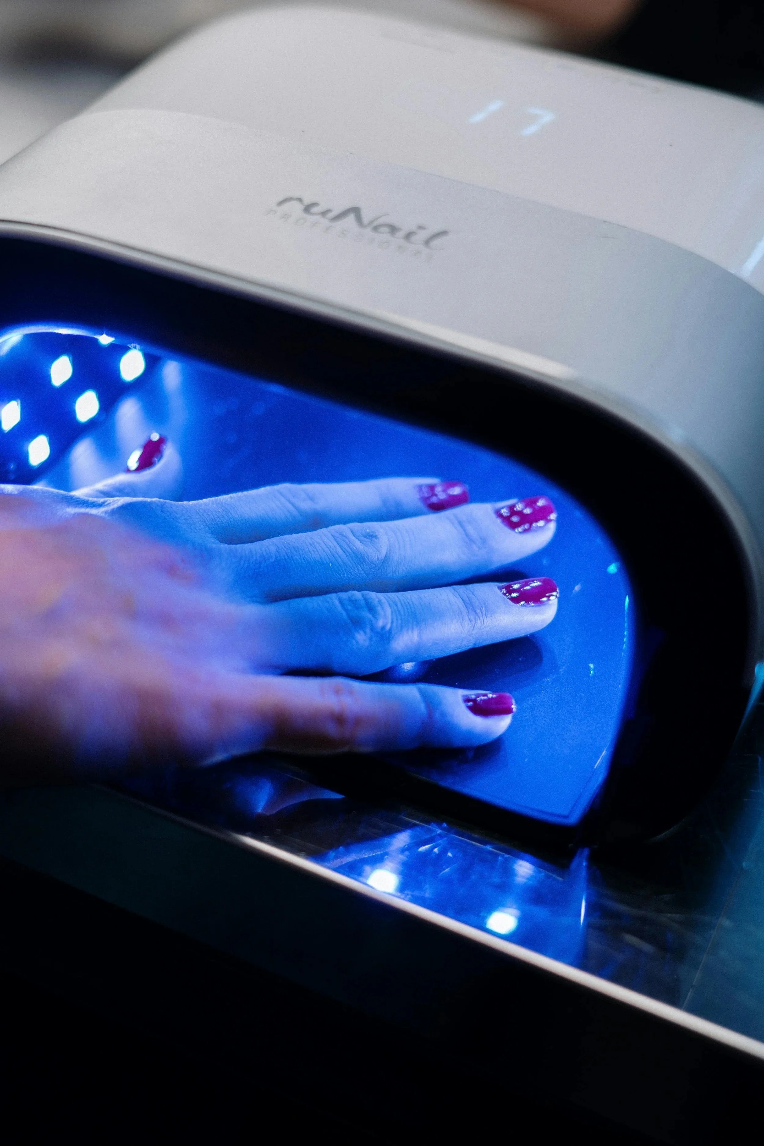 Hand with painted nails under a blue UV light inside a nail curing device.
